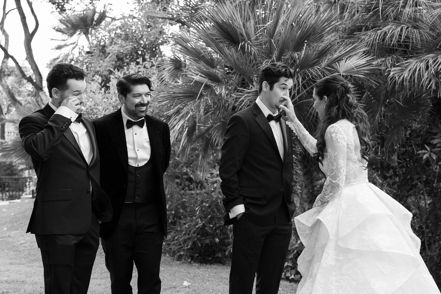 Wedding party poses together outdoors with palm trees in background.