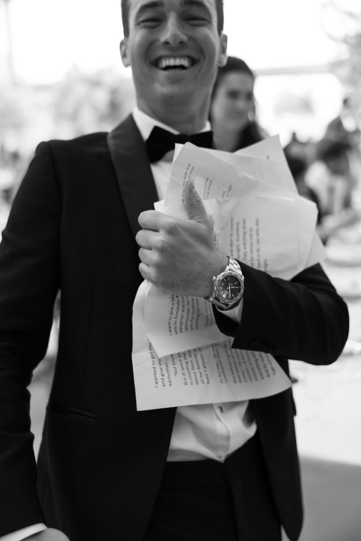 Black and white photo of guests laughing while reading papers at formal event.