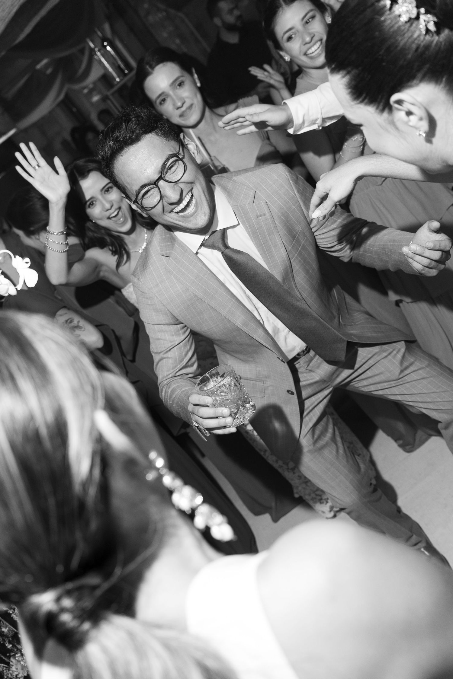 Black and white photo of wedding guests dancing and celebrating at a reception.