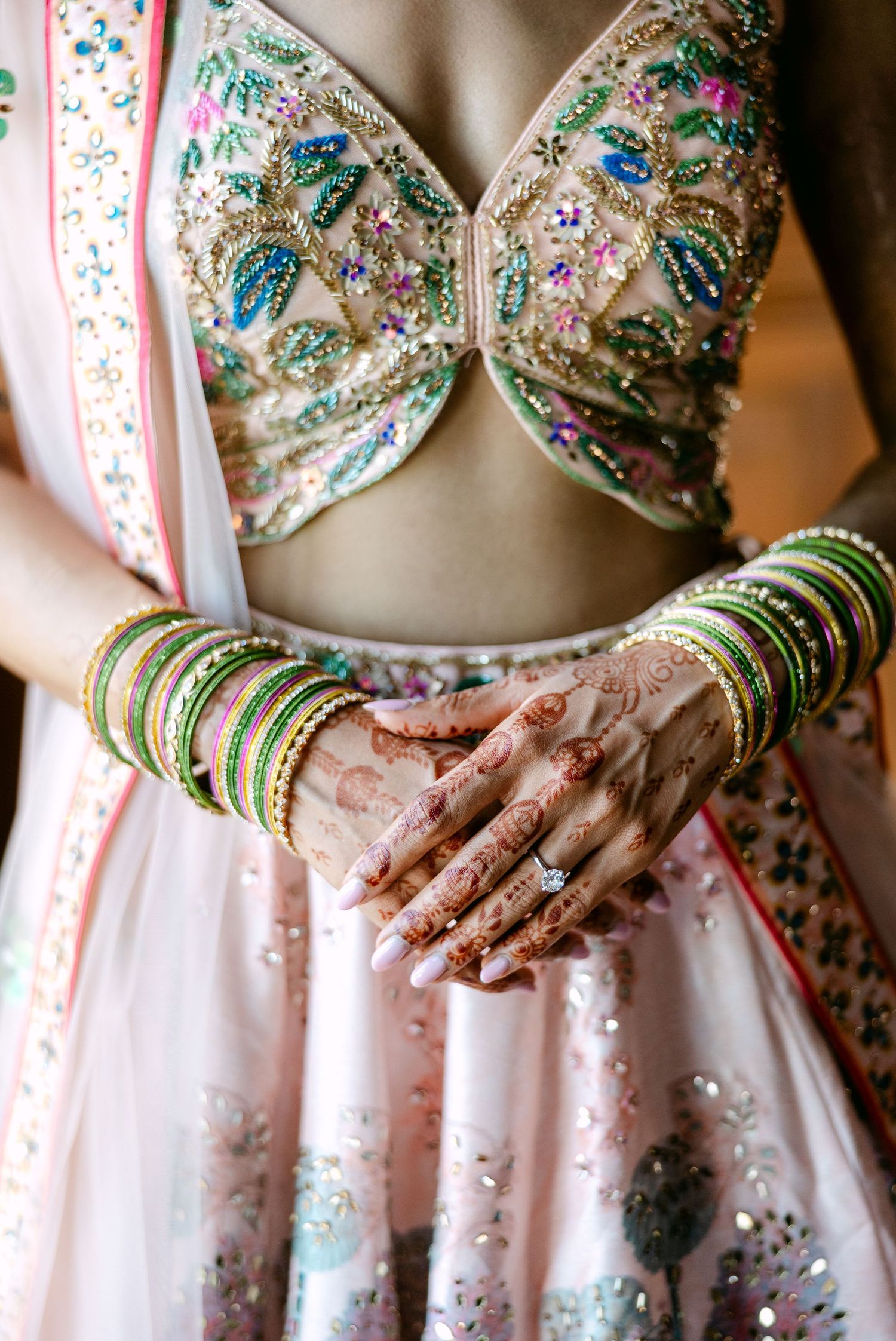 Close-up of traditional Indian bridal lehenga with detailed embroidery and bangles.