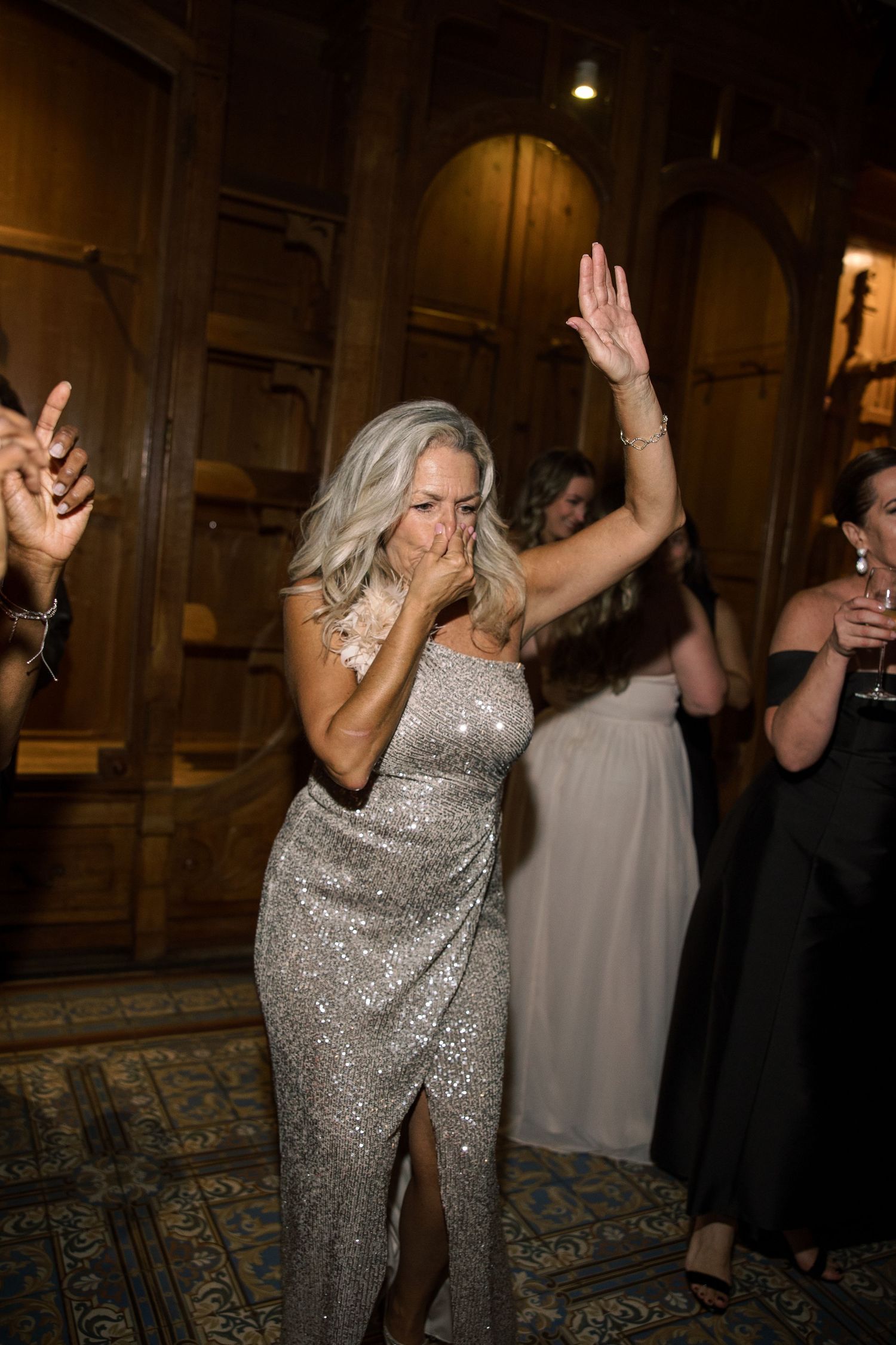 Woman in sparkly silver dress dances energetically at evening celebration.