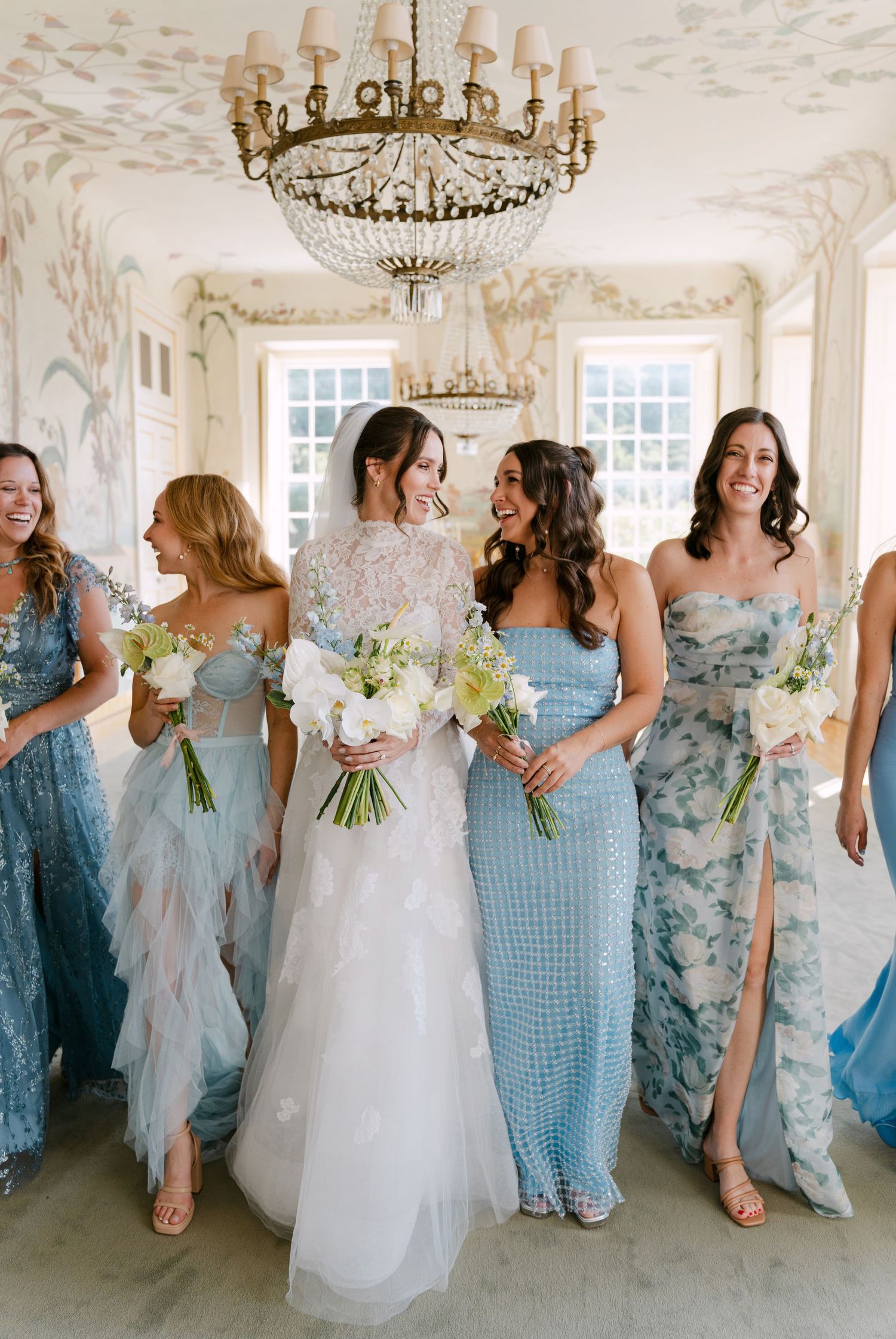 Bridesmaids in light blue dresses pose with bride in an ornate white room.