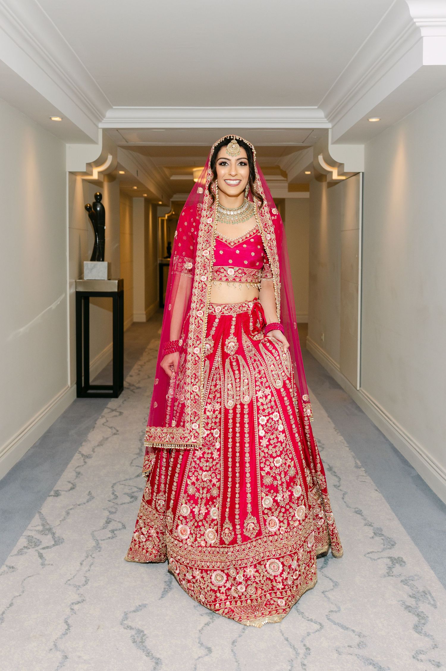 Traditional red bridal lehenga with intricate gold embroidery in an elegant hallway.