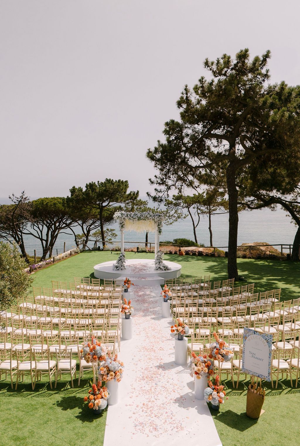 Outdoor wedding ceremony setup with white chairs and floral aisle decorations overlooking the ocean.