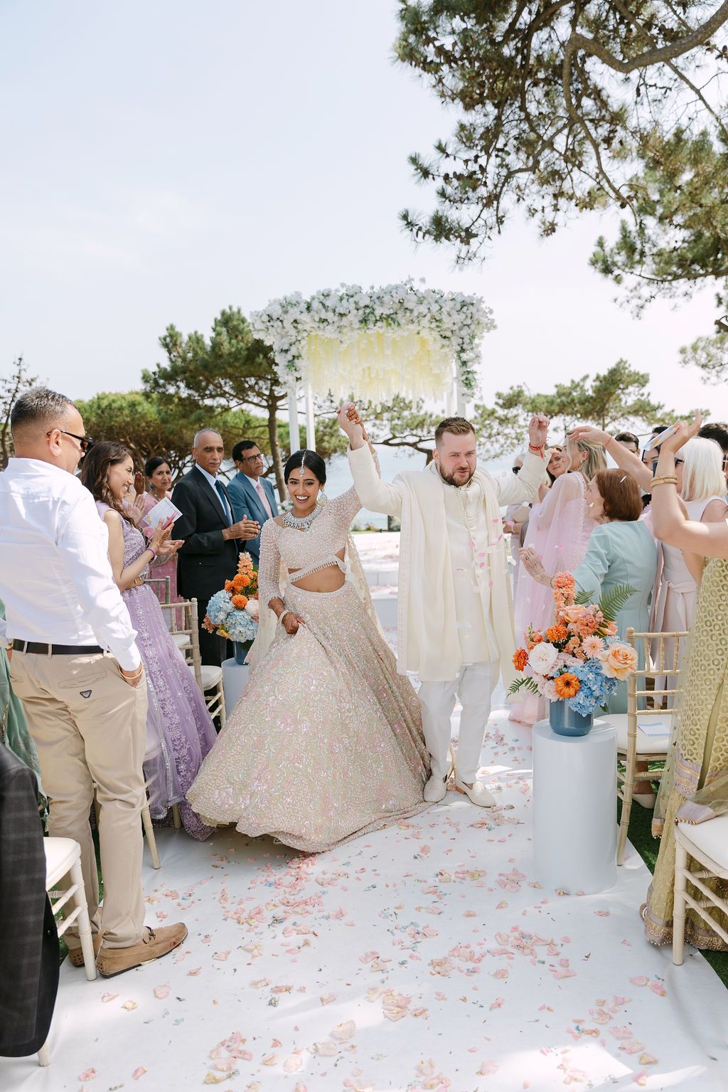 Wedding guests celebrate on a flower petal-covered dance floor at an outdoor reception.