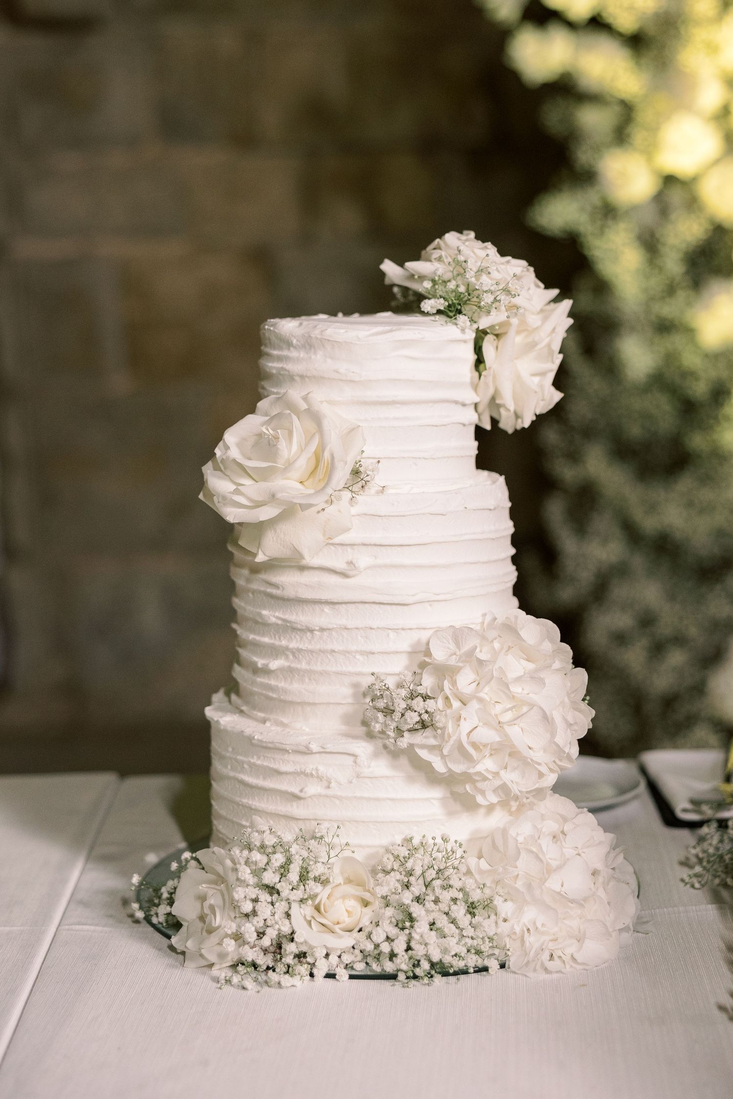 Elegant white wedding cake decorated with roses and delicate floral accents on a rustic table.
