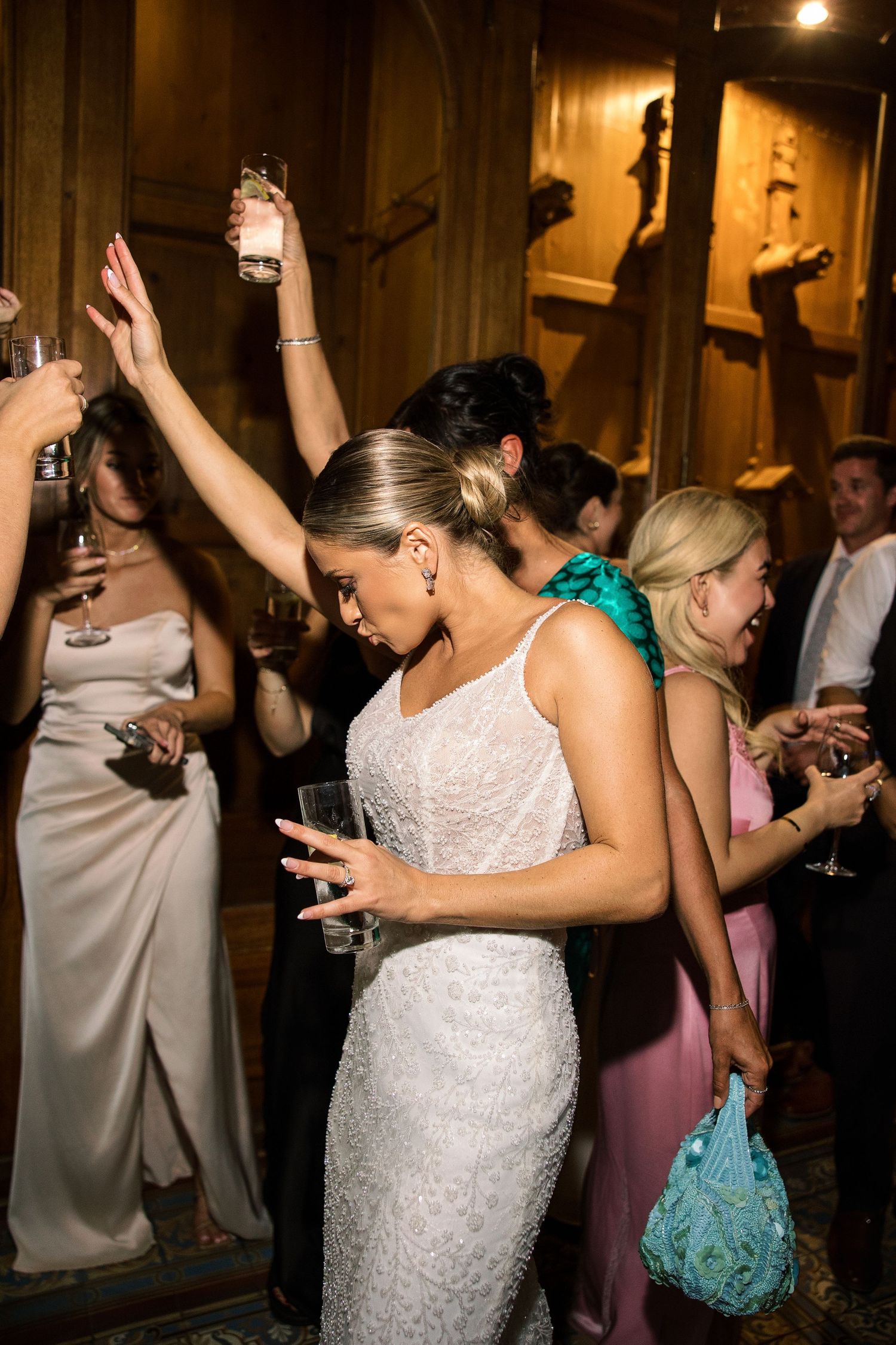 Wedding party dancing enthusiastically at indoor reception with festive lighting.