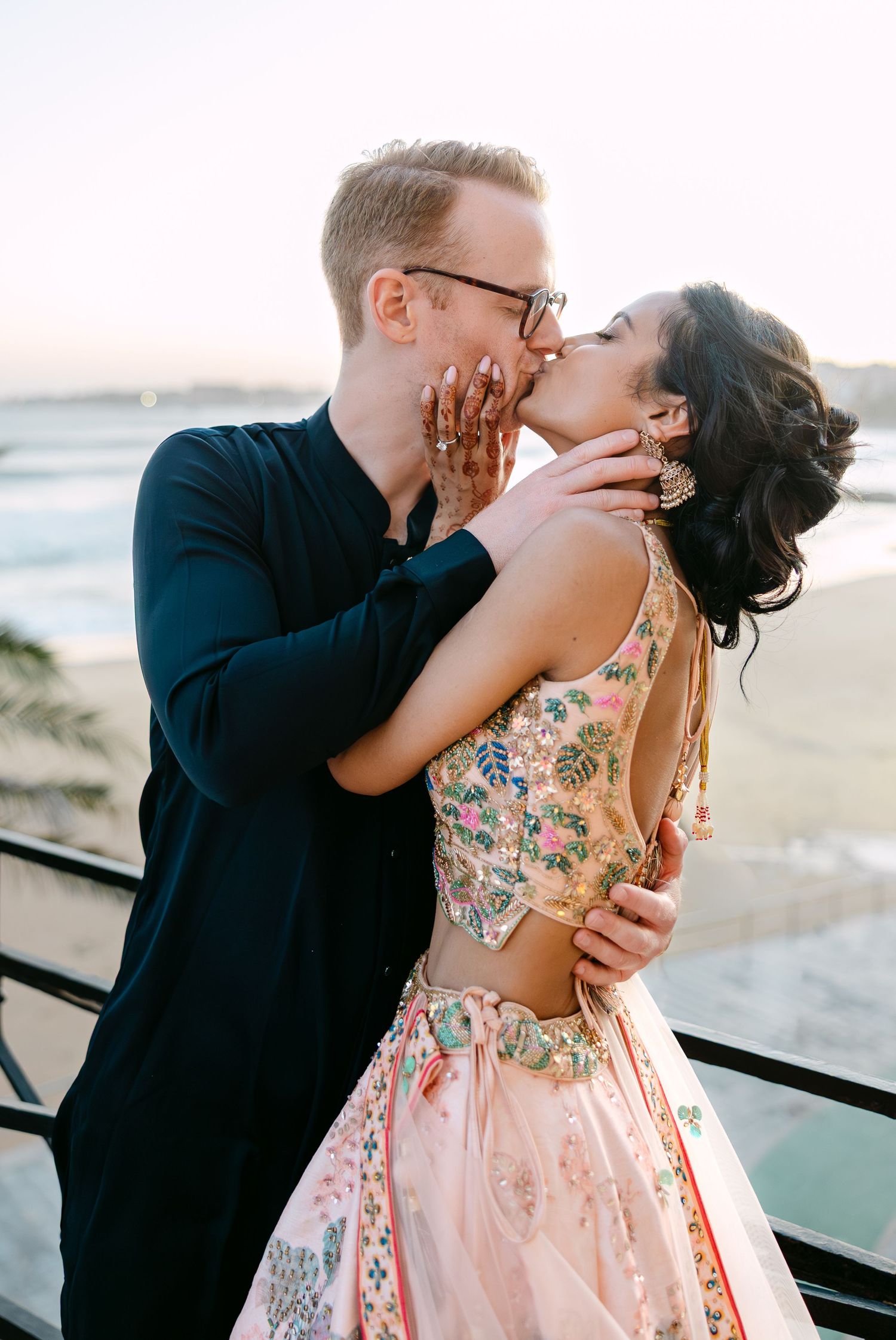 Romantic sunset kiss between couple with ocean backdrop and soft natural lighting.