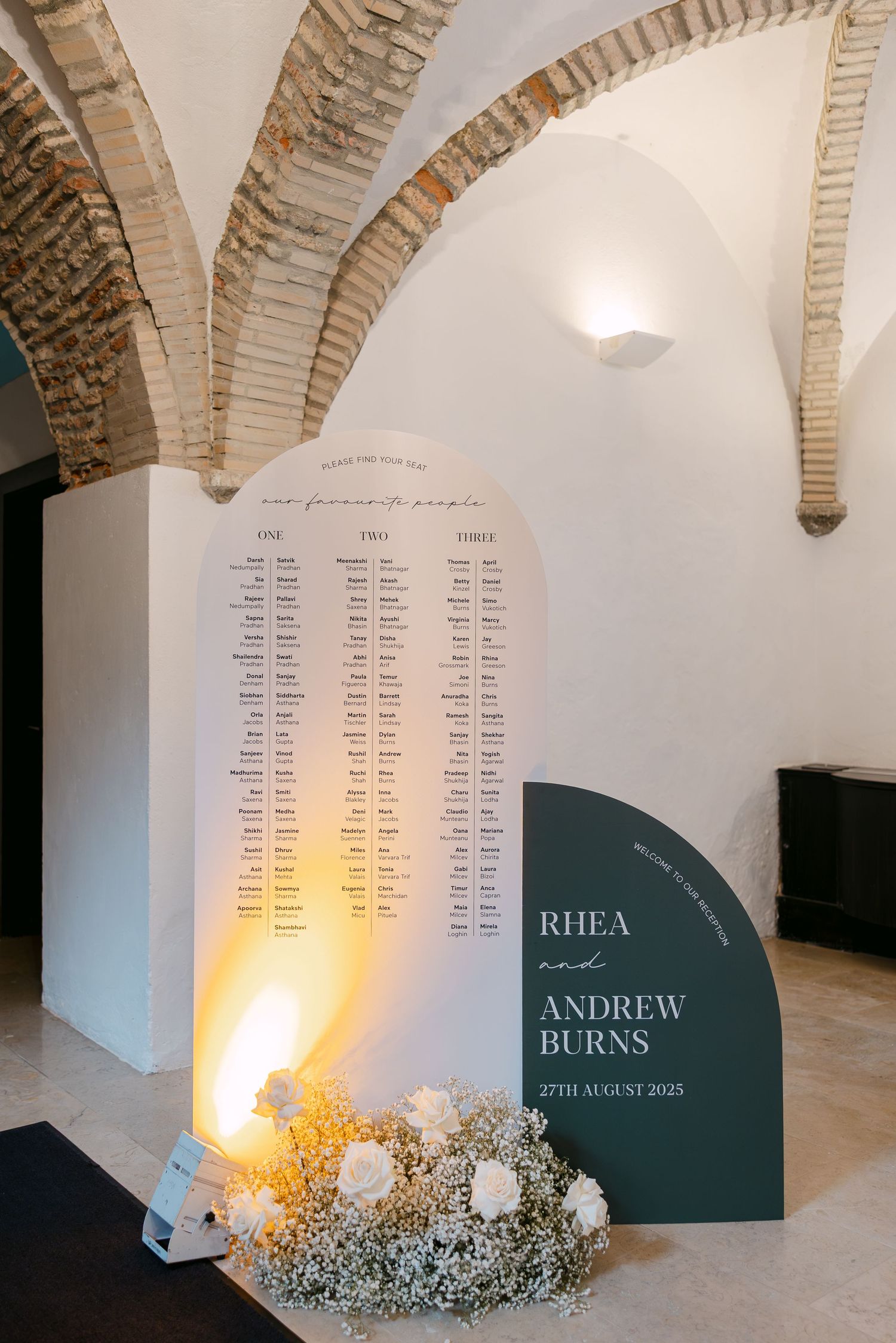 Wedding seating chart display with floral decorations under rustic brick arches.