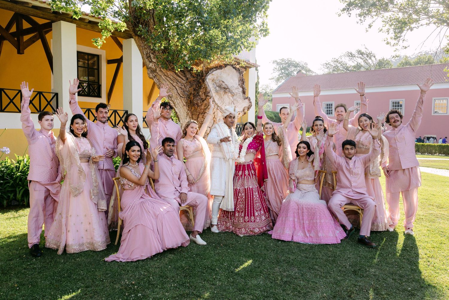 Wedding group photo session with attendees in pink and red traditional attire outdoors.