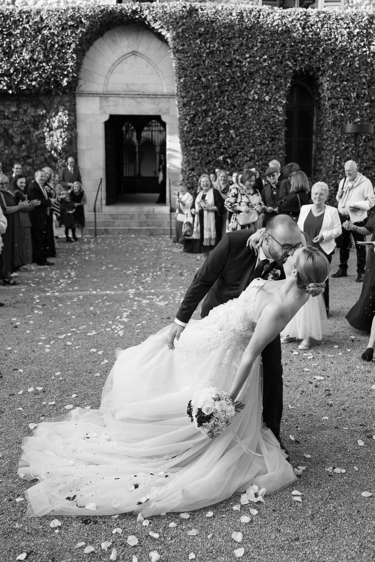 A wedding couple twirls and dances on a garden lawn with flower petals scattered around them.