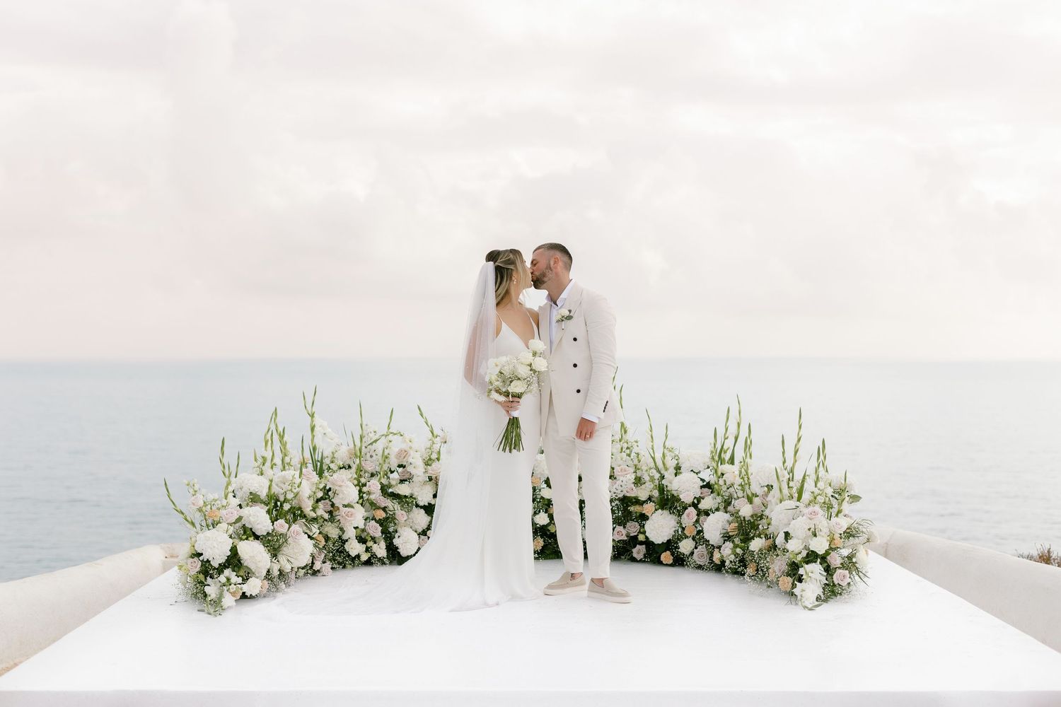 Minimalist white beach wedding ceremony setup with floral arrangements.