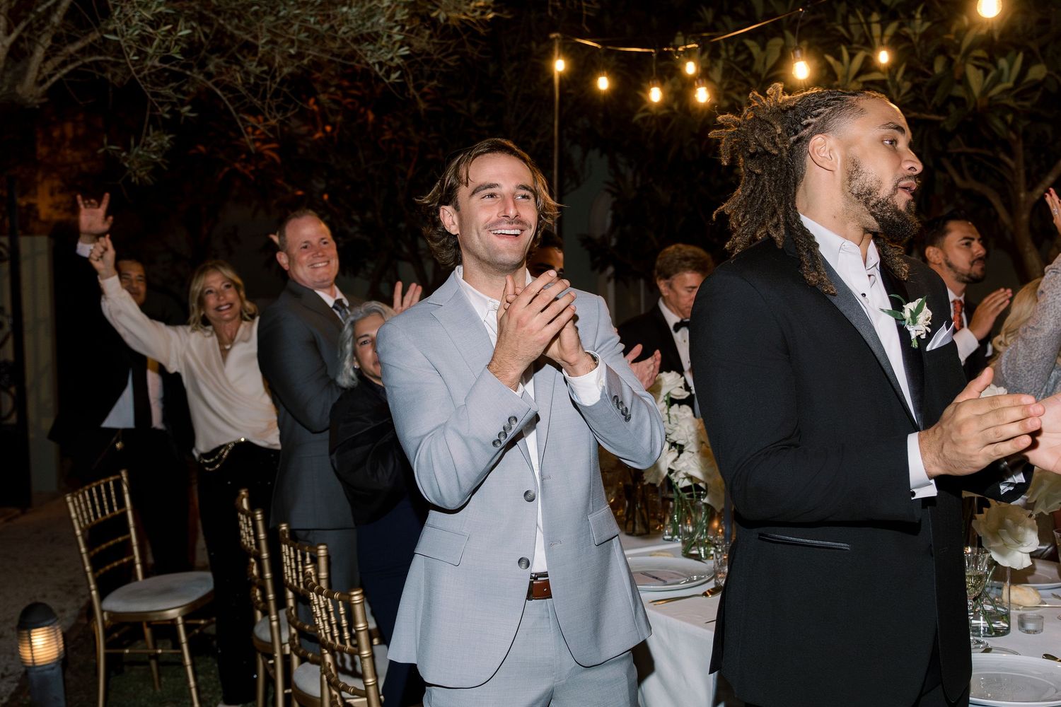 Wedding guests celebrating under warm string lights at outdoor reception.