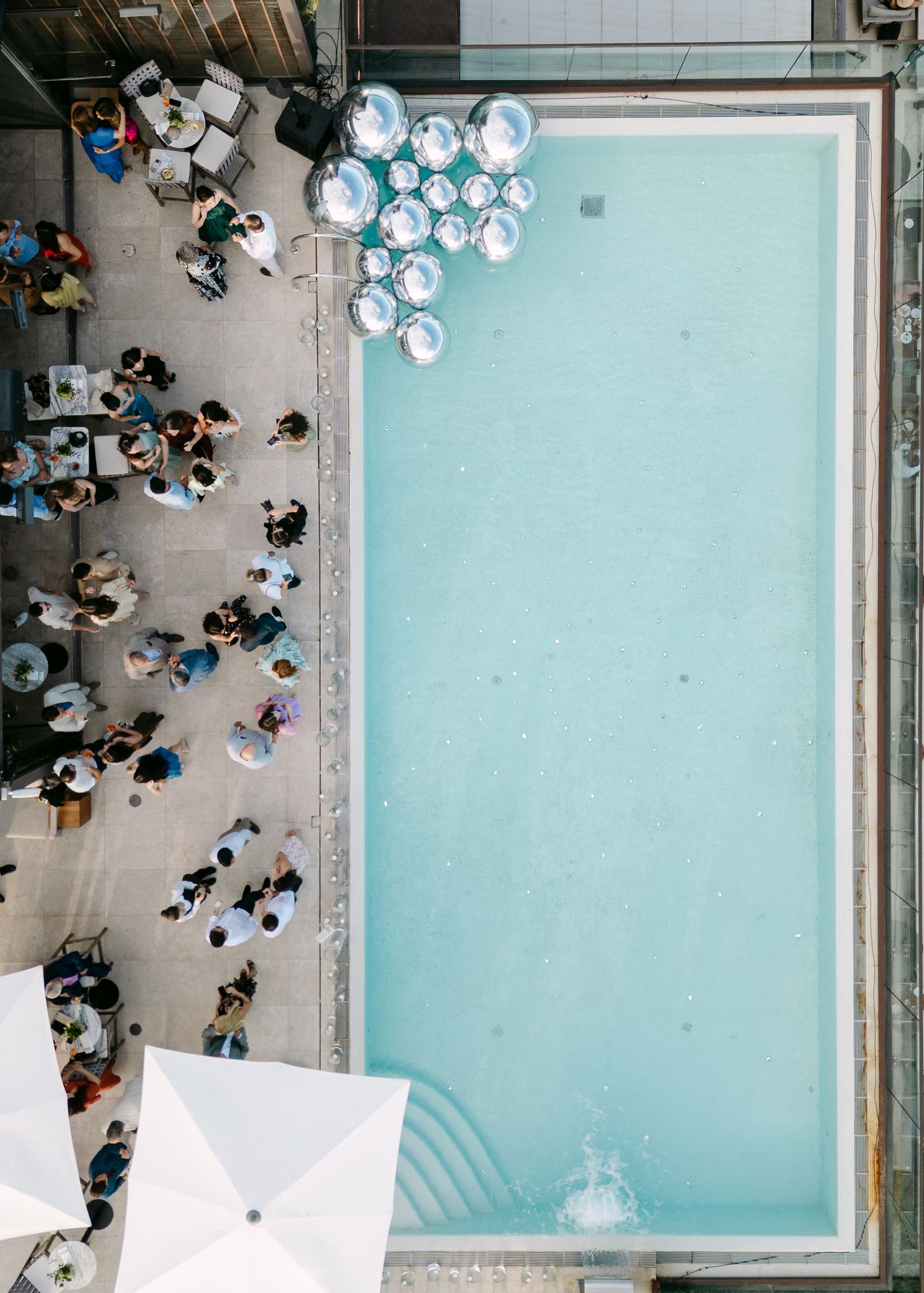 Aerial view of a modern swimming pool with geometric white umbrellas and lounging guests.