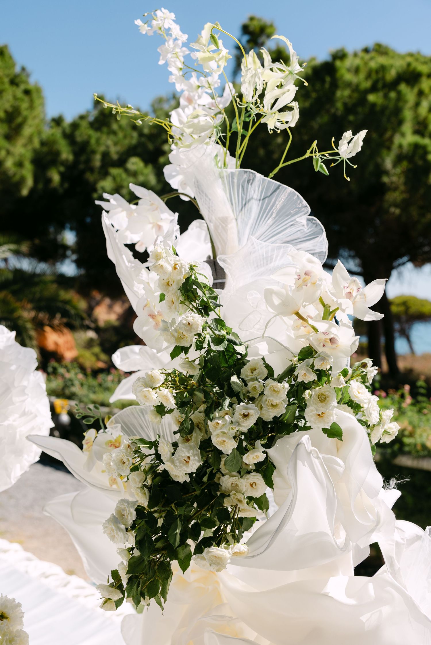 Elegant white floral arrangement with delicate petals and greenery against a garden backdrop.