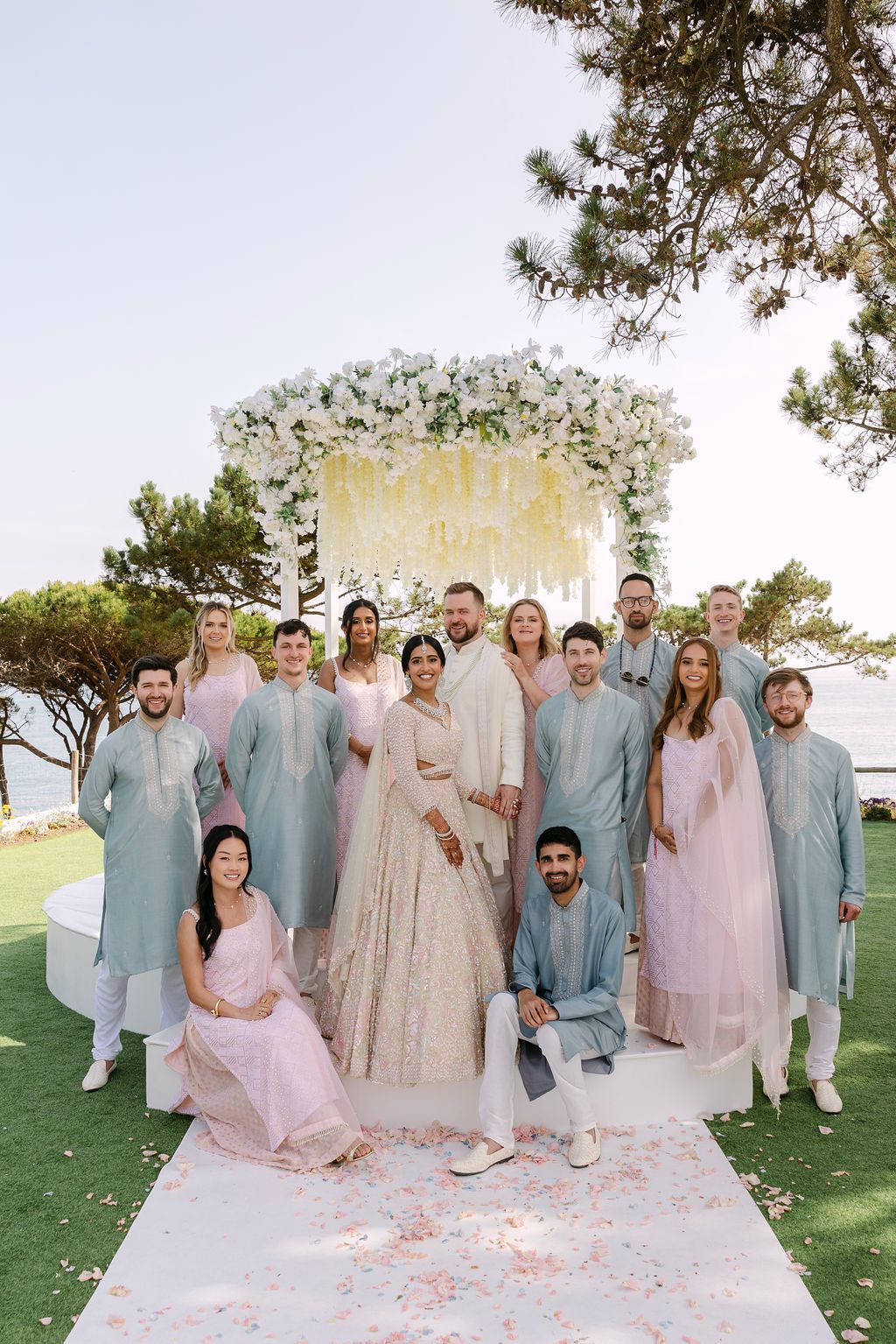 Wedding party in coordinated pastel blue and pink outfits posing on a grassy lawn.