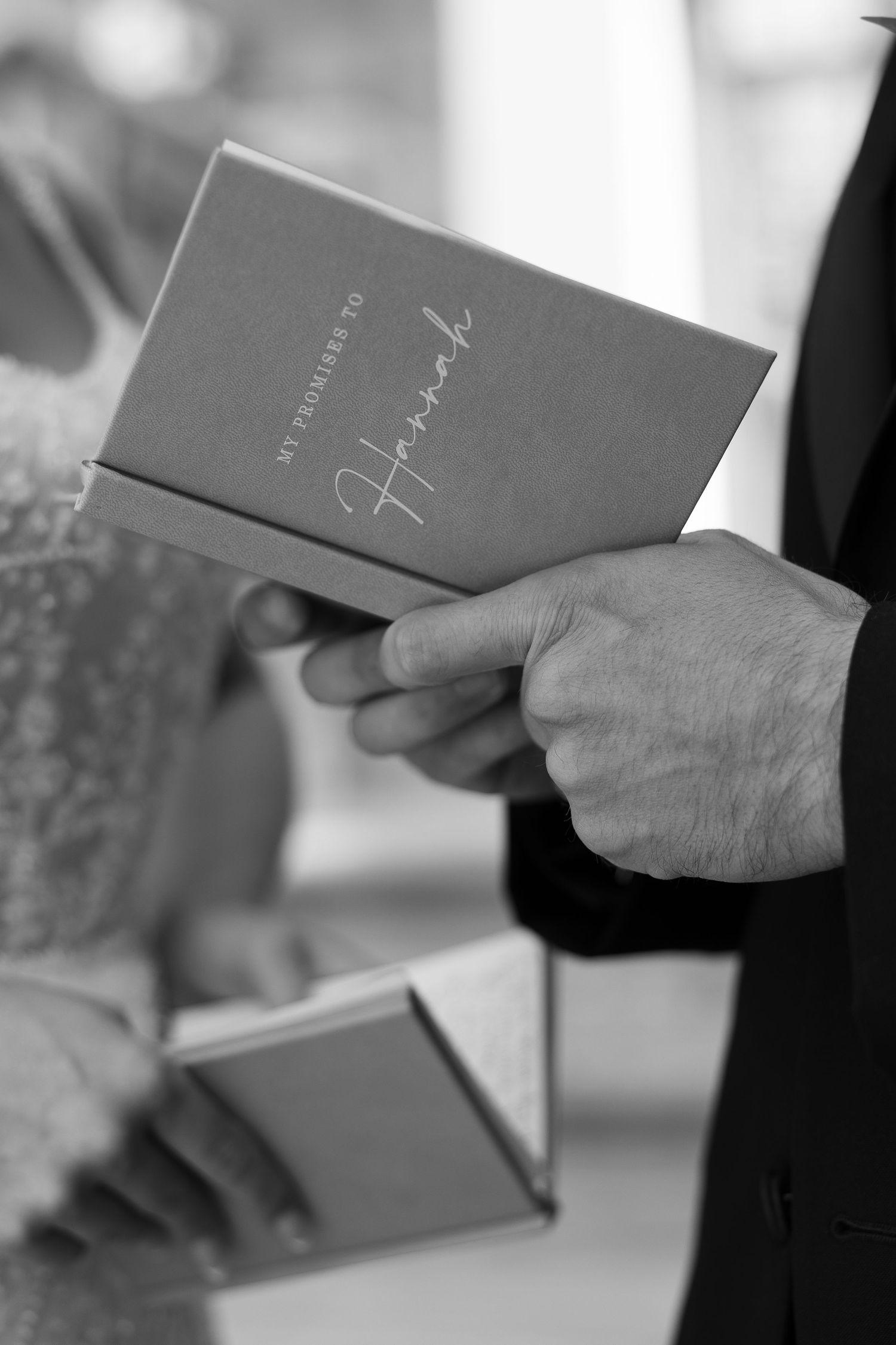 Black and white detail shots of wedding vow books being held.