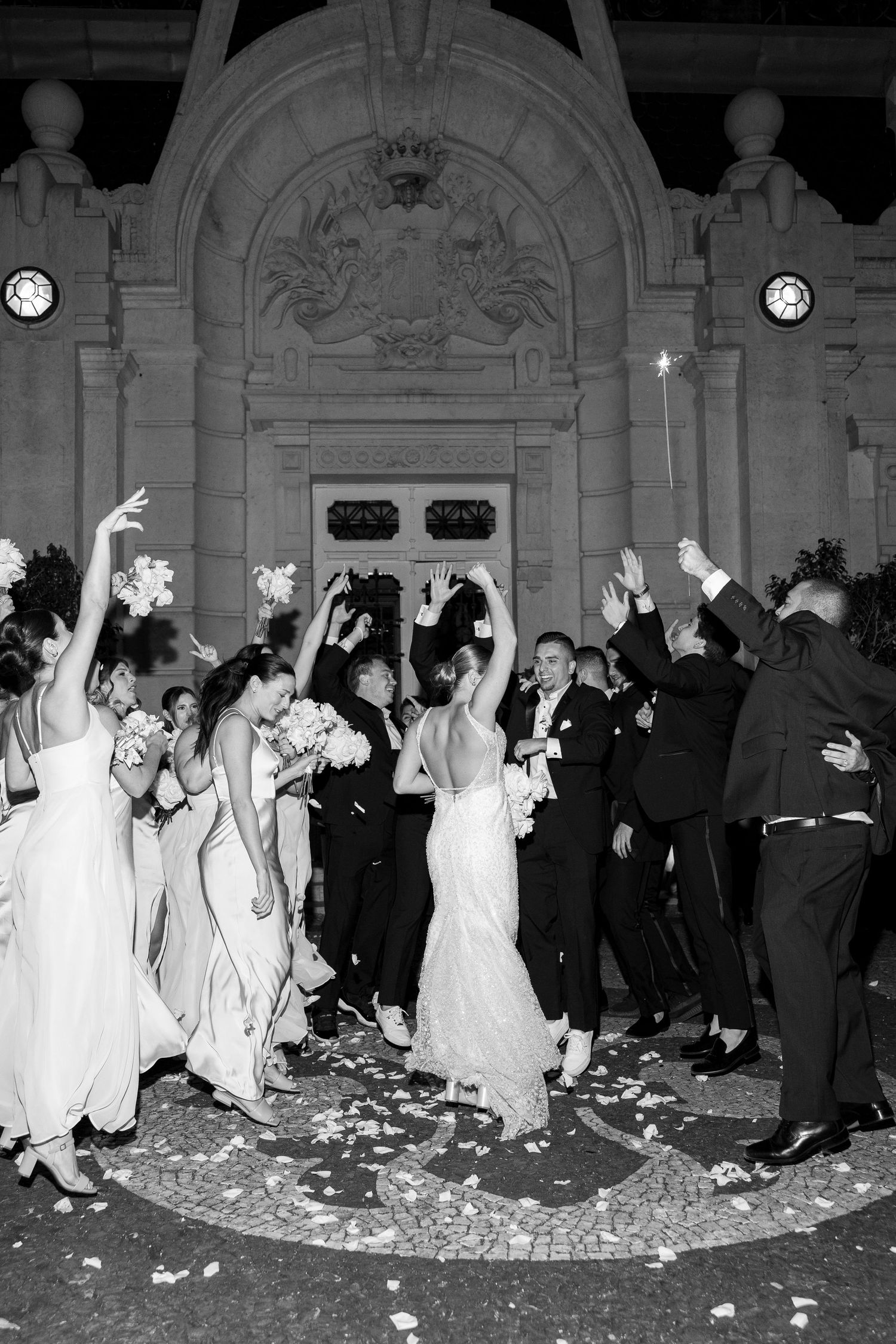 Wedding party dancing in formal attire with confetti scattered on the ballroom floor.