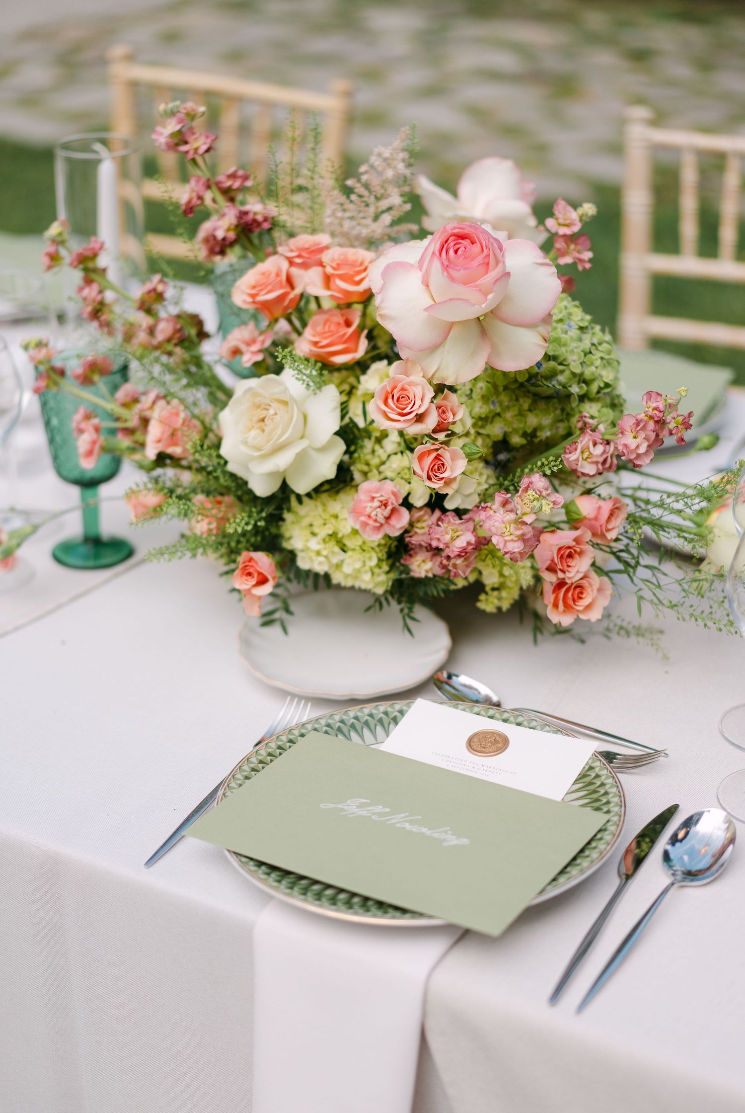 Romantic table setting with pink and coral floral centerpieces and sage green accents.