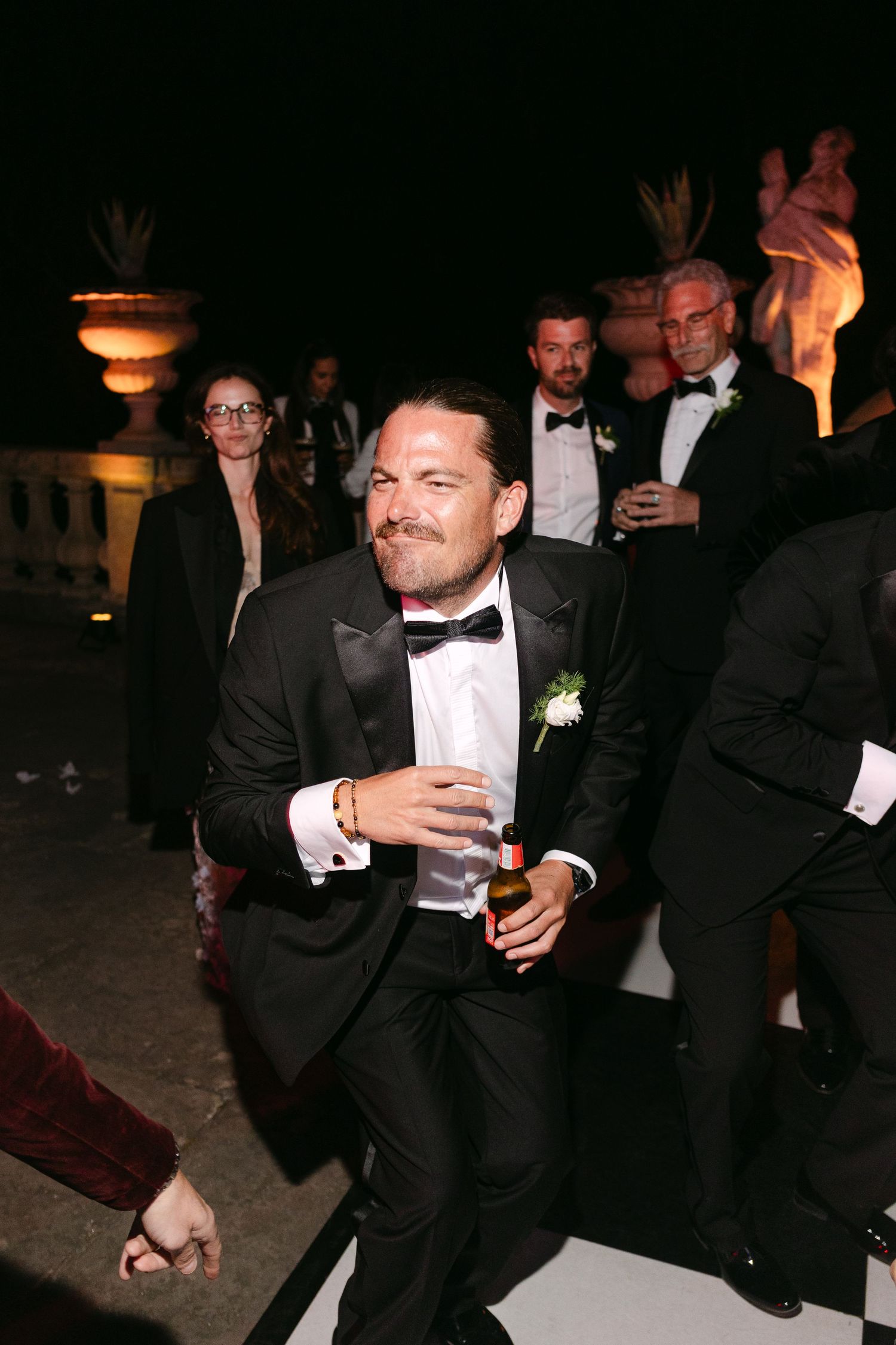 Wedding guest in tuxedo dancing and smiling at an outdoor evening wedding reception.