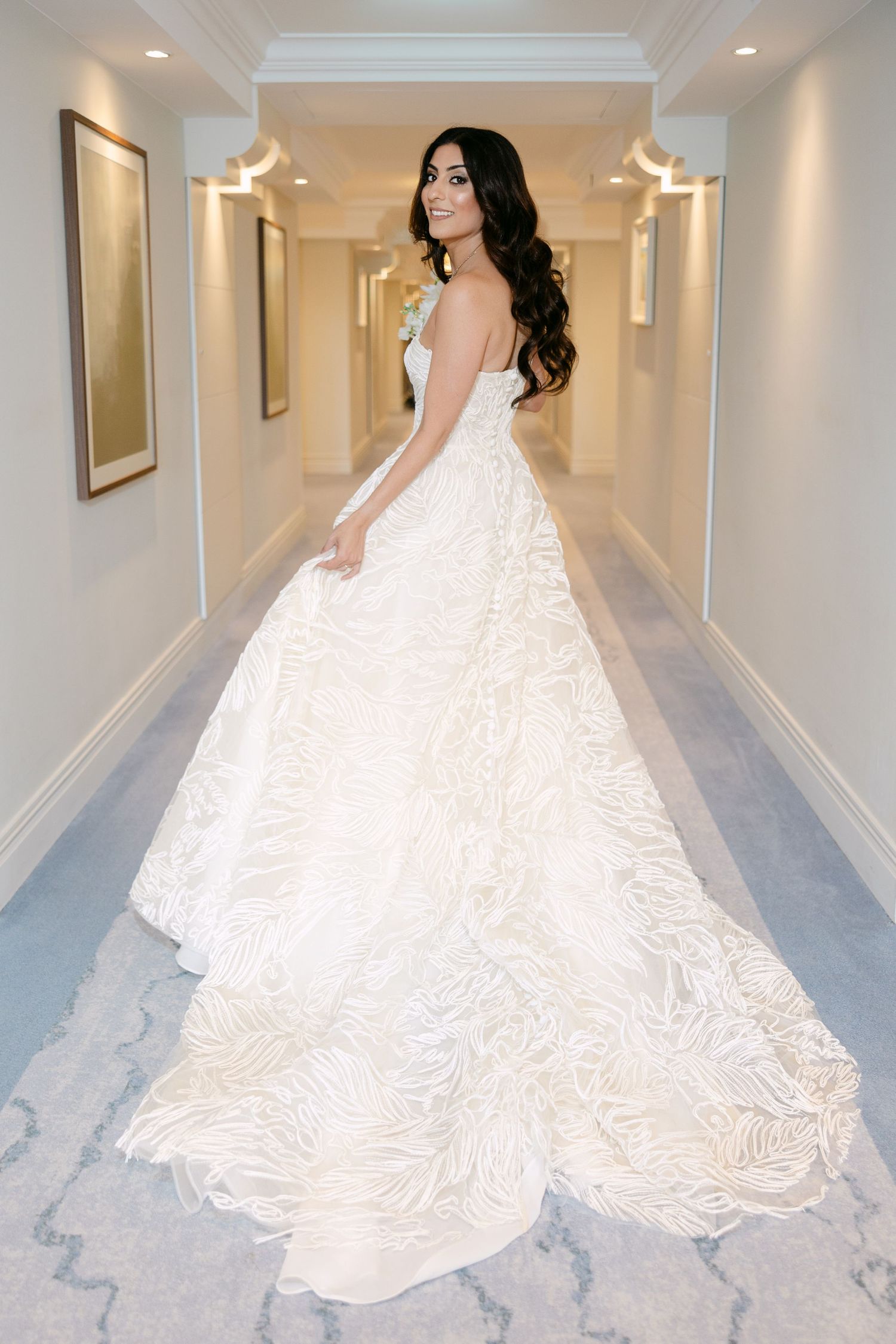 Bride in flowing white ballgown photographed dramatically in elegant hotel hallway.