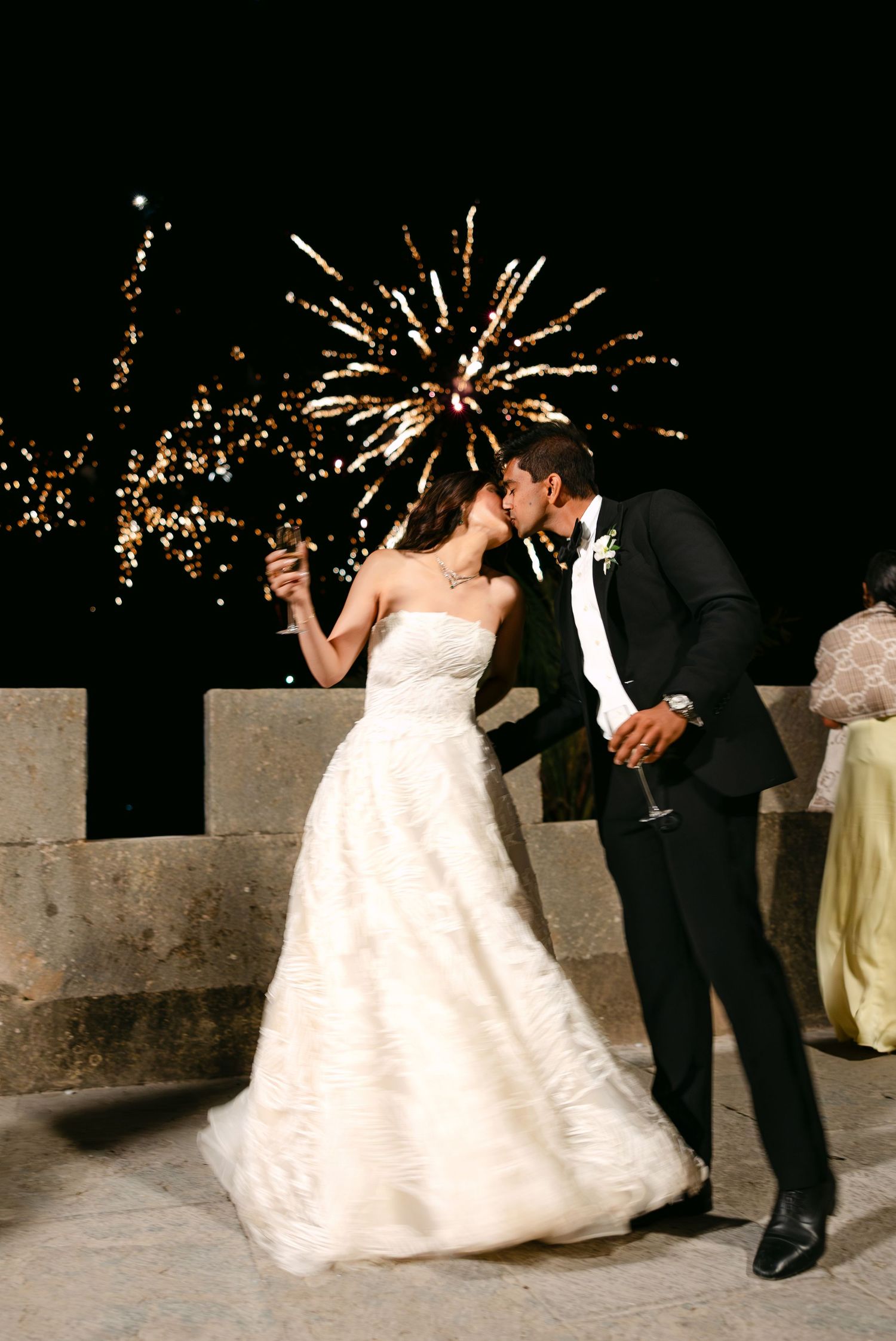 Romantic couple shares intimate moment under fireworks display at nighttime wedding celebration.