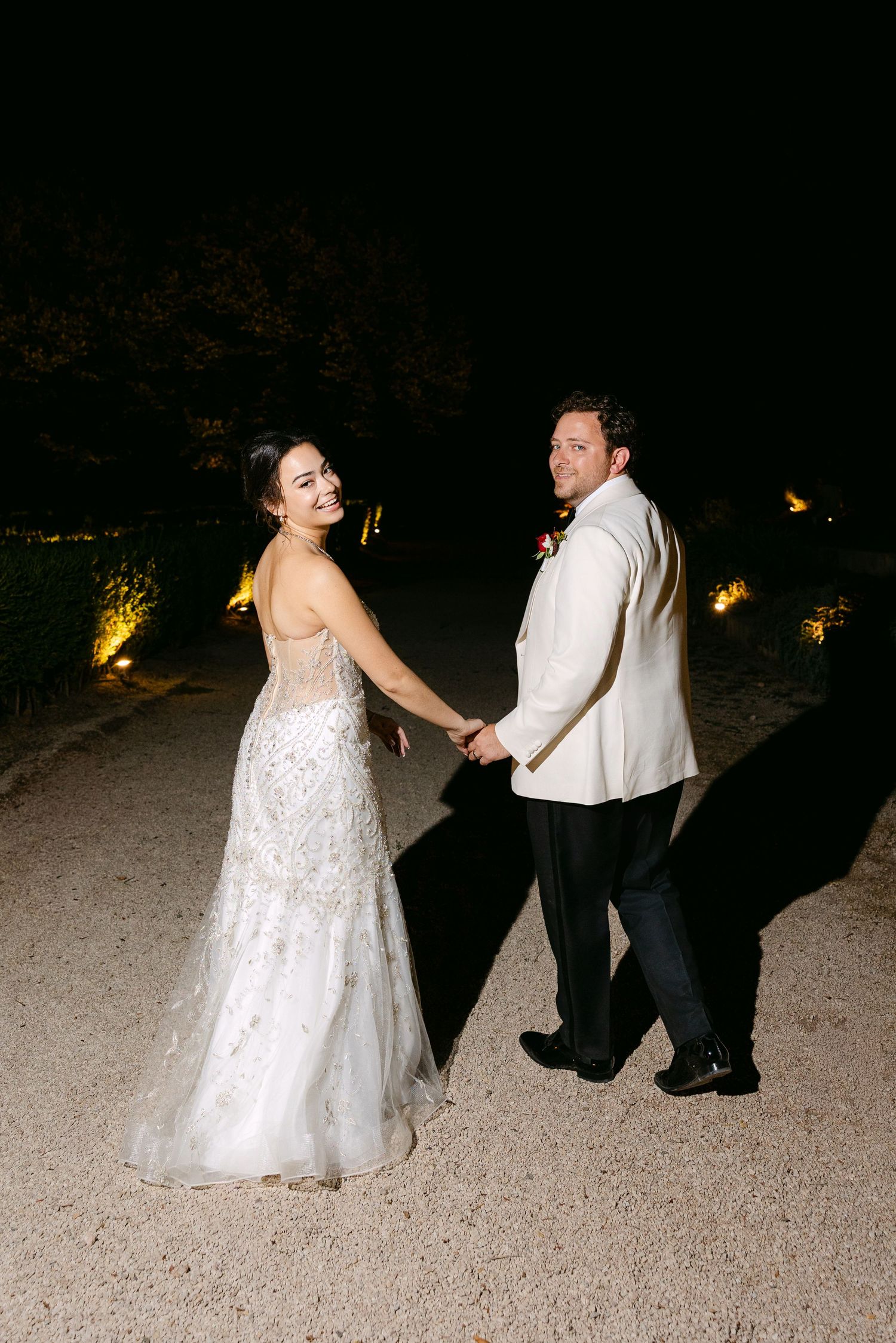 A couple in wedding attire performs a playful dance sequence on a sandy beach at night.