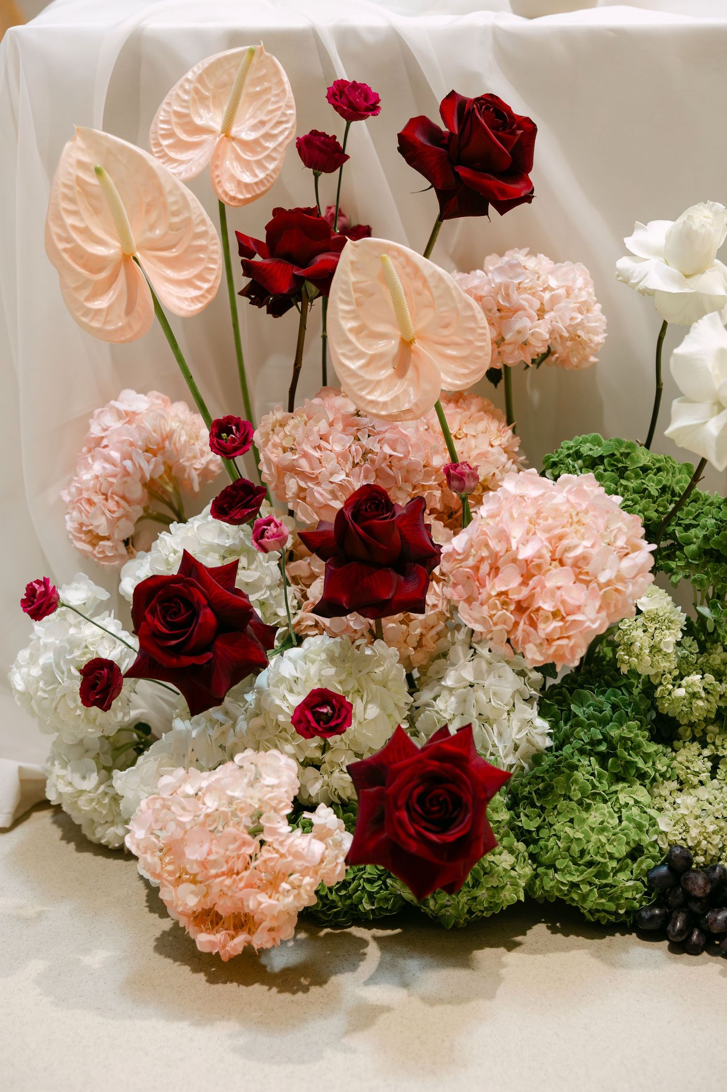 Elegant floral arrangement featuring pink anthuriums, deep red roses, light pink carnations, and white hydrangeas.