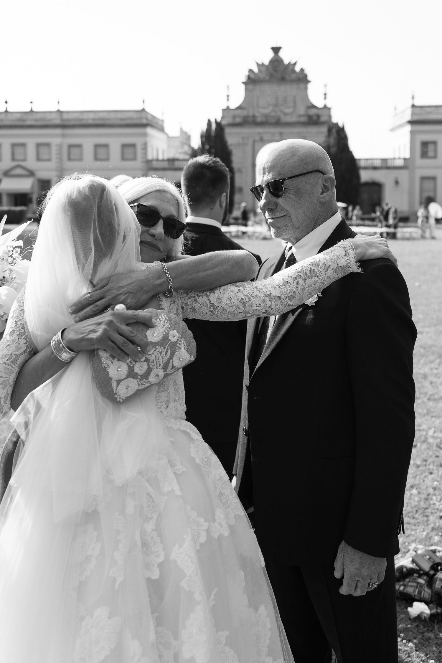 Wedding couple shares playful moment with guests in formal attire outdoors.