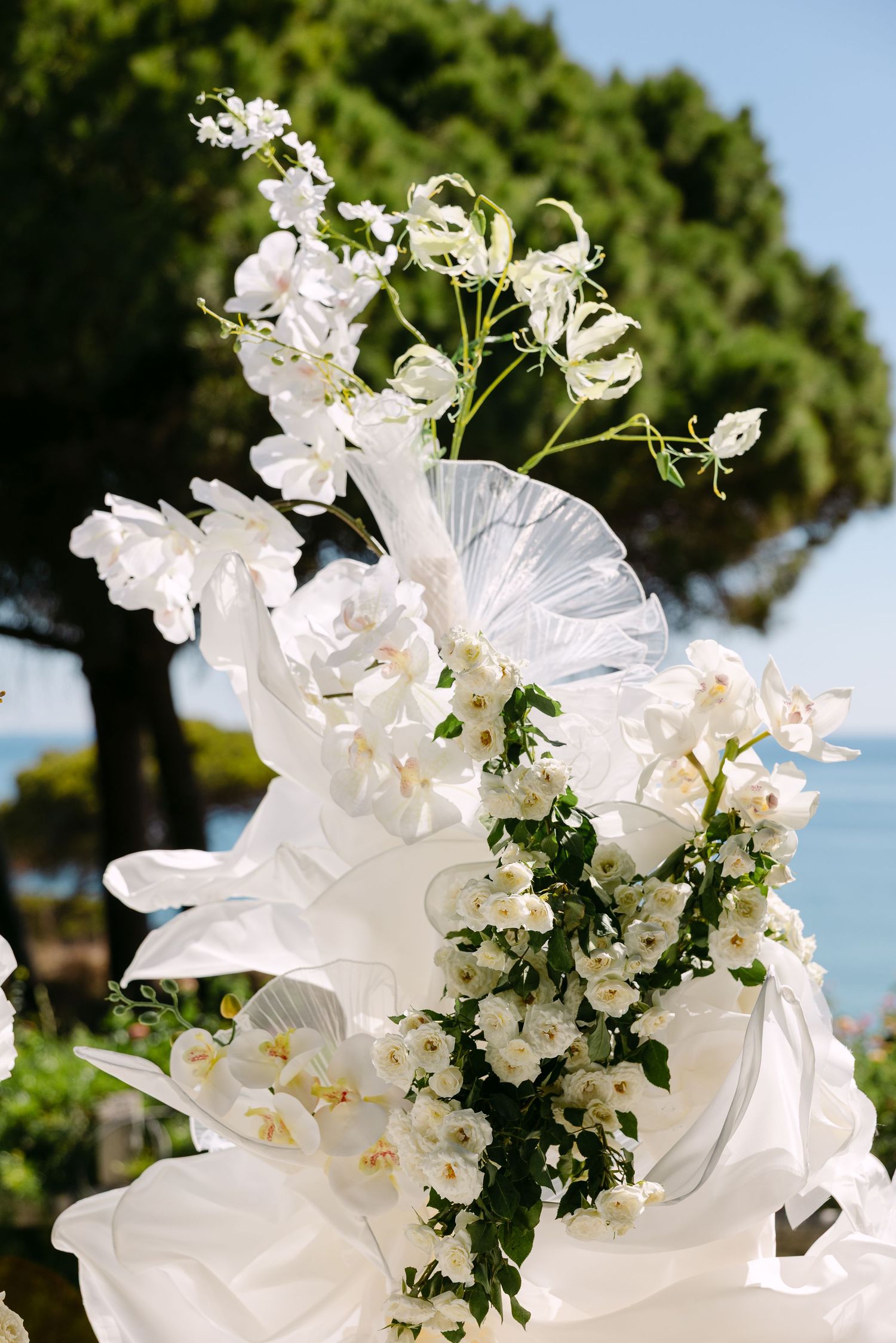 White floral wedding arch arrangements against a blue sky with trees in the background.
