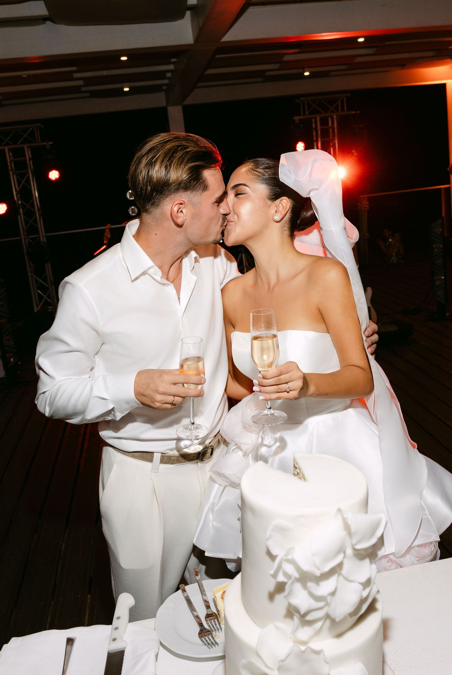 Couple in white sharing intimate moment with champagne glasses.