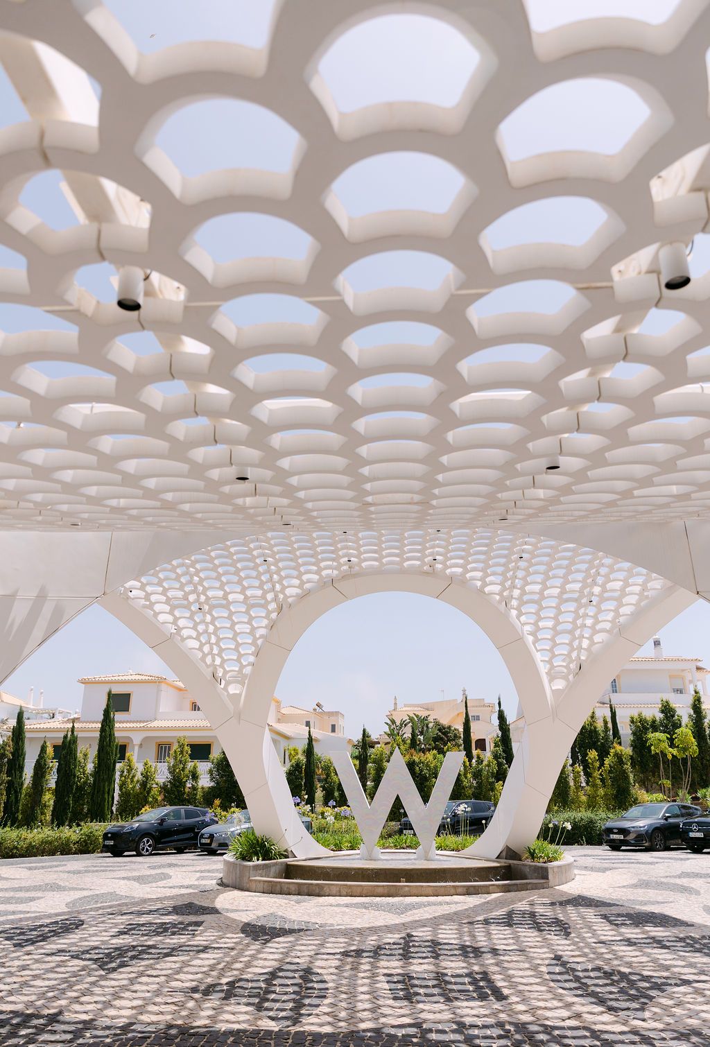Modern white architectural structure with geometric lattice ceiling and arched openings.