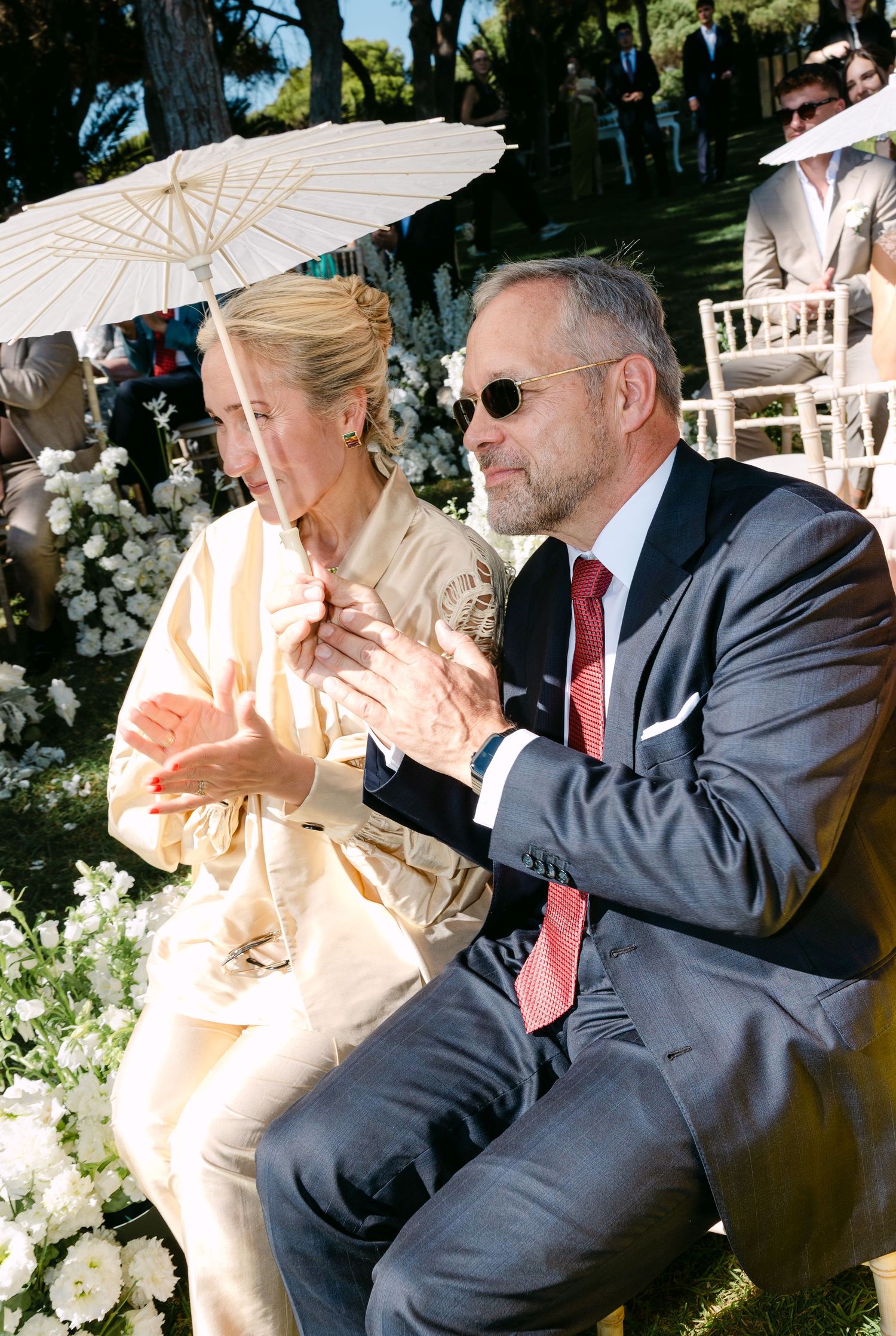 Wedding guests seated with parasols during an outdoor ceremony.