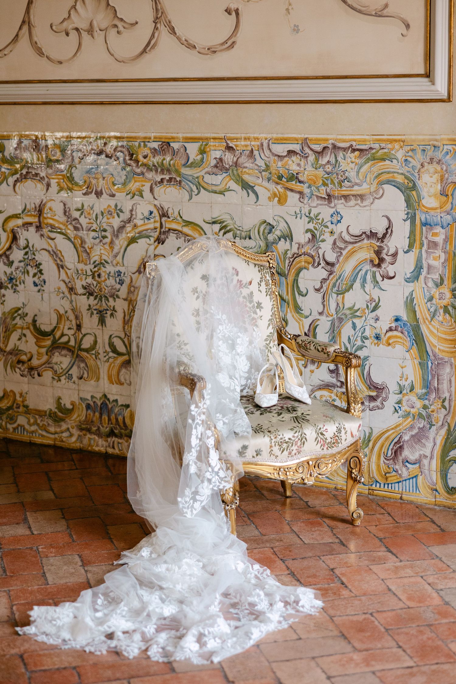 A flowing white wedding dress train laid out on ornate terracotta tiles with decorative wall details.