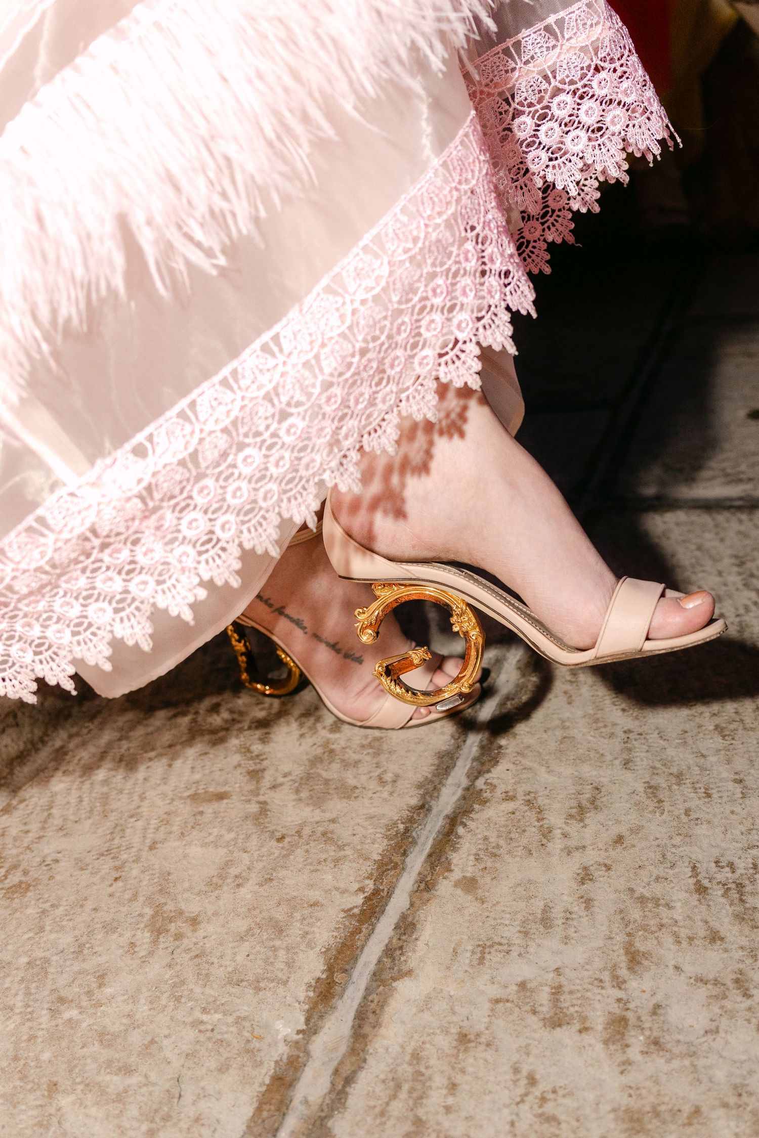 Close-up shots of pink lace dress hem and nude heels on stone floor.