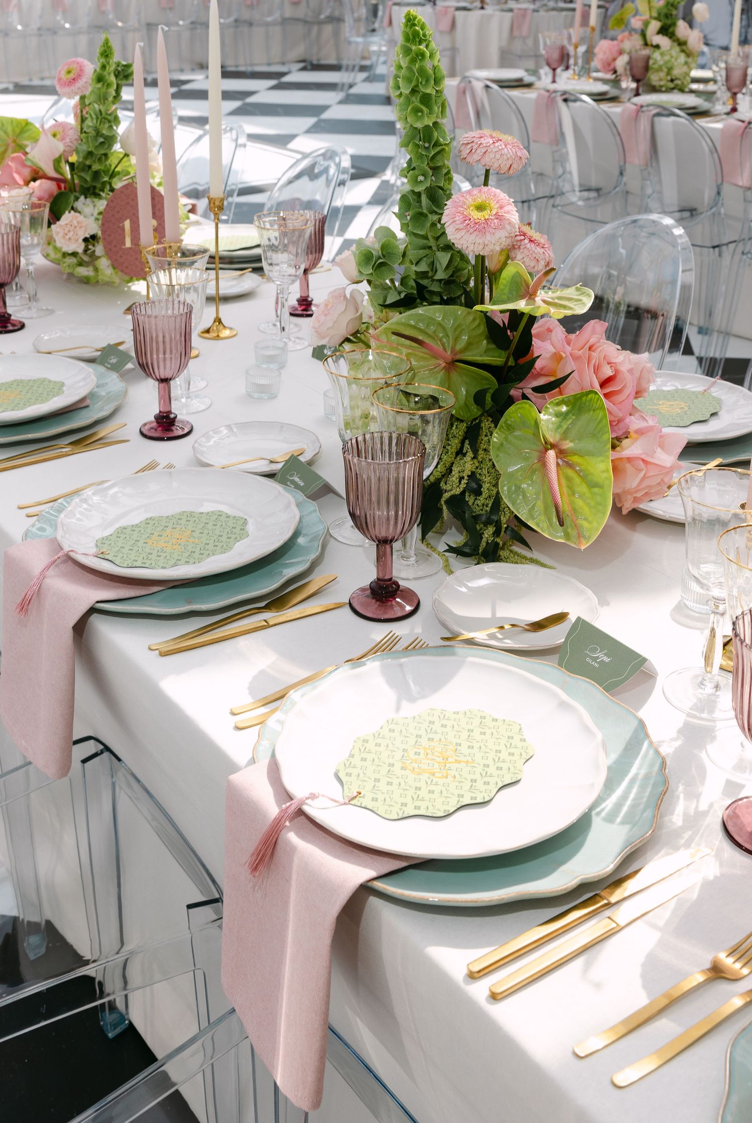 Wedding table settings with pink napkins, gold flatware, and floral centerpieces.