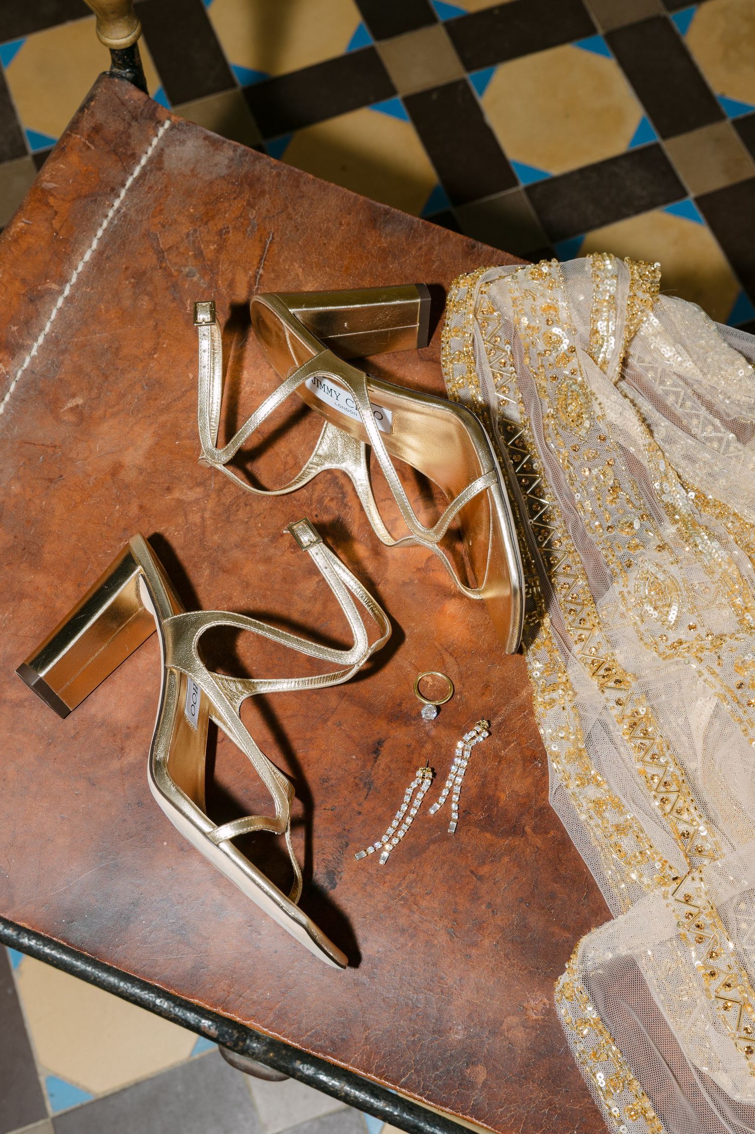 Elegant gold high heels and jewelry displayed on a vintage leather surface with checkerboard floor.