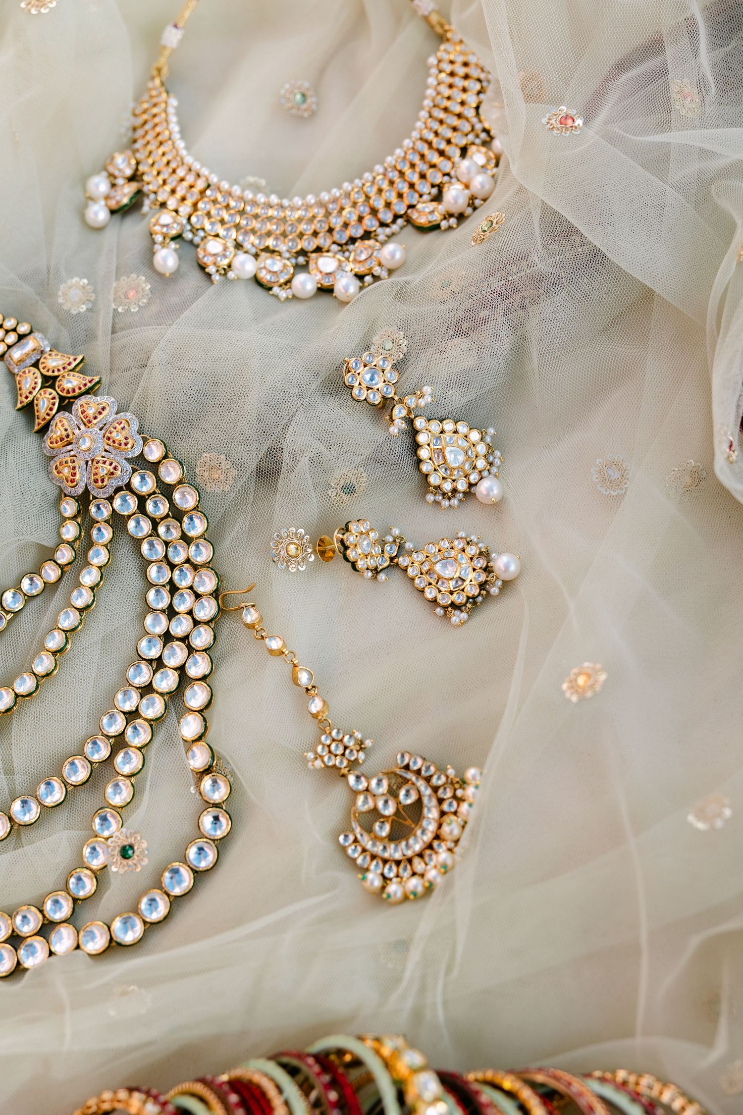 Ornate Indian bridal jewelry with pearls and crystals laid out on tulle fabric.