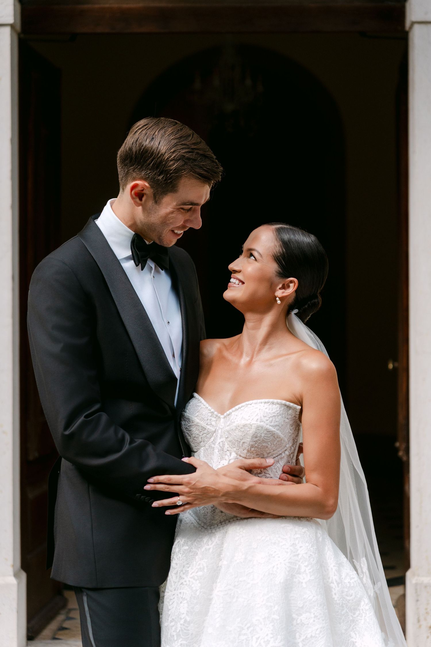 Joyful moment captured between couple in formal wedding attire under arched doorway.