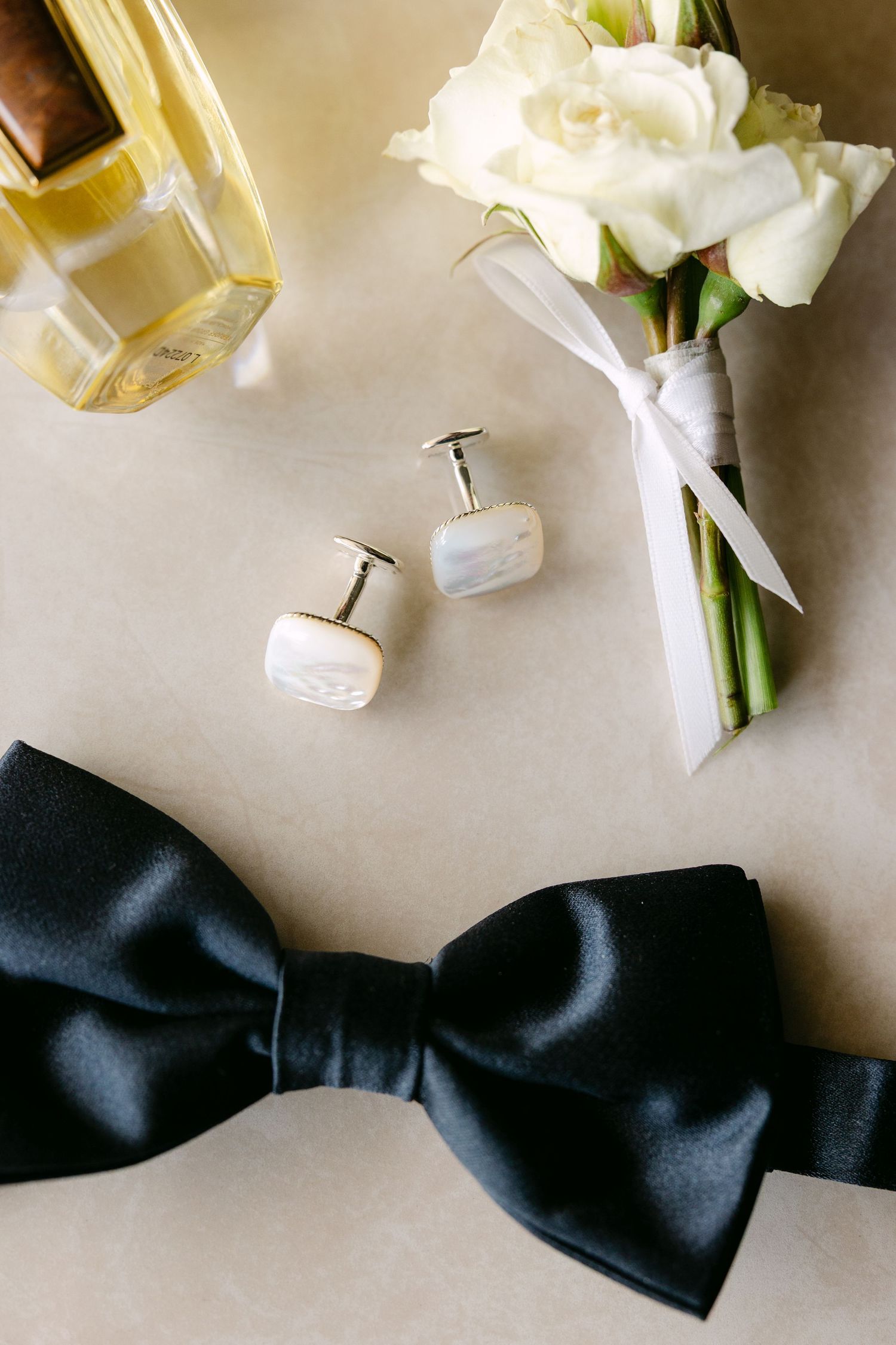 White rose boutonnieres and black bow tie arranged on light beige surface.