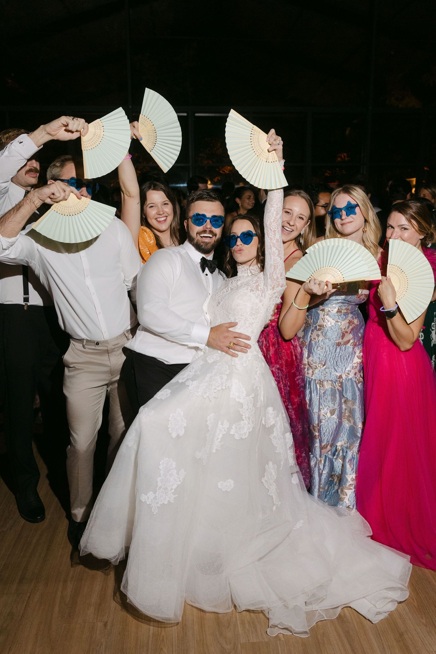 Wedding reception party guests posing with decorative white paper fans.