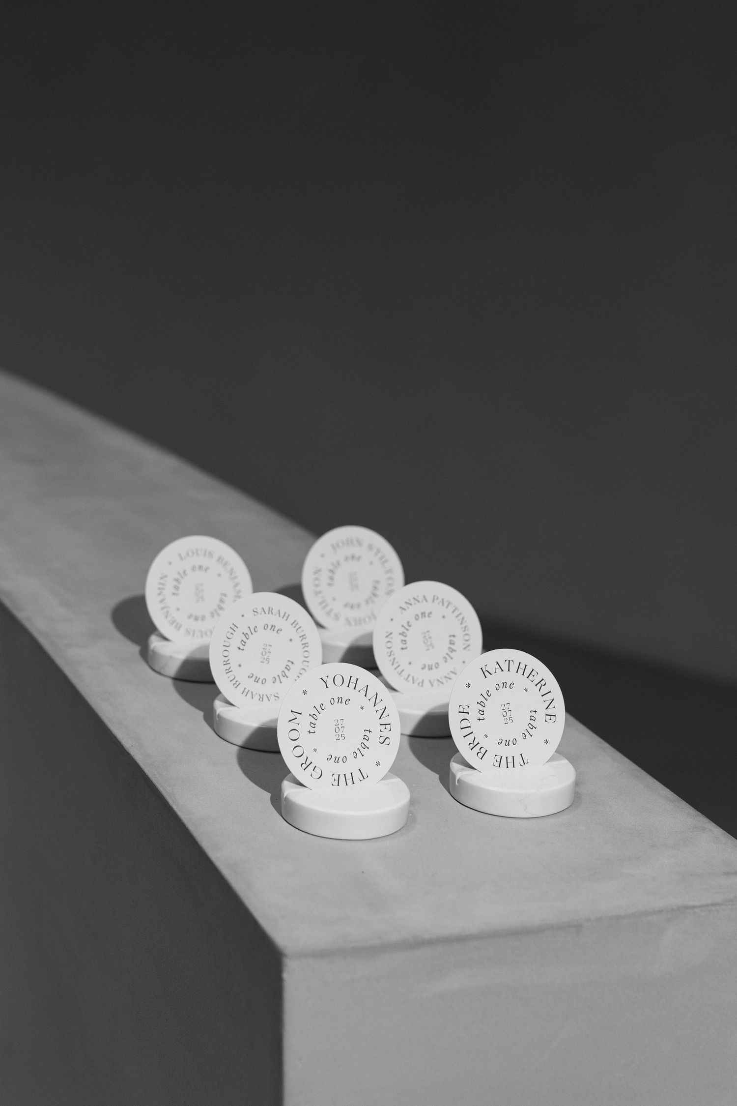 Black and white photo of circular white place cards displayed on stands arranged on a wooden ledge.