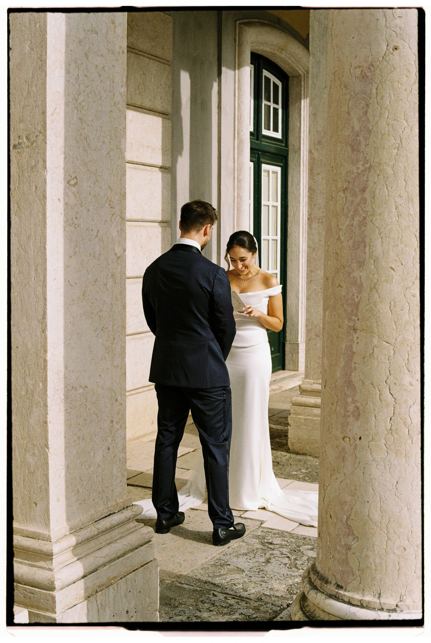 Bride and groom share a private moment between stone columns at an elegant wedding venue.