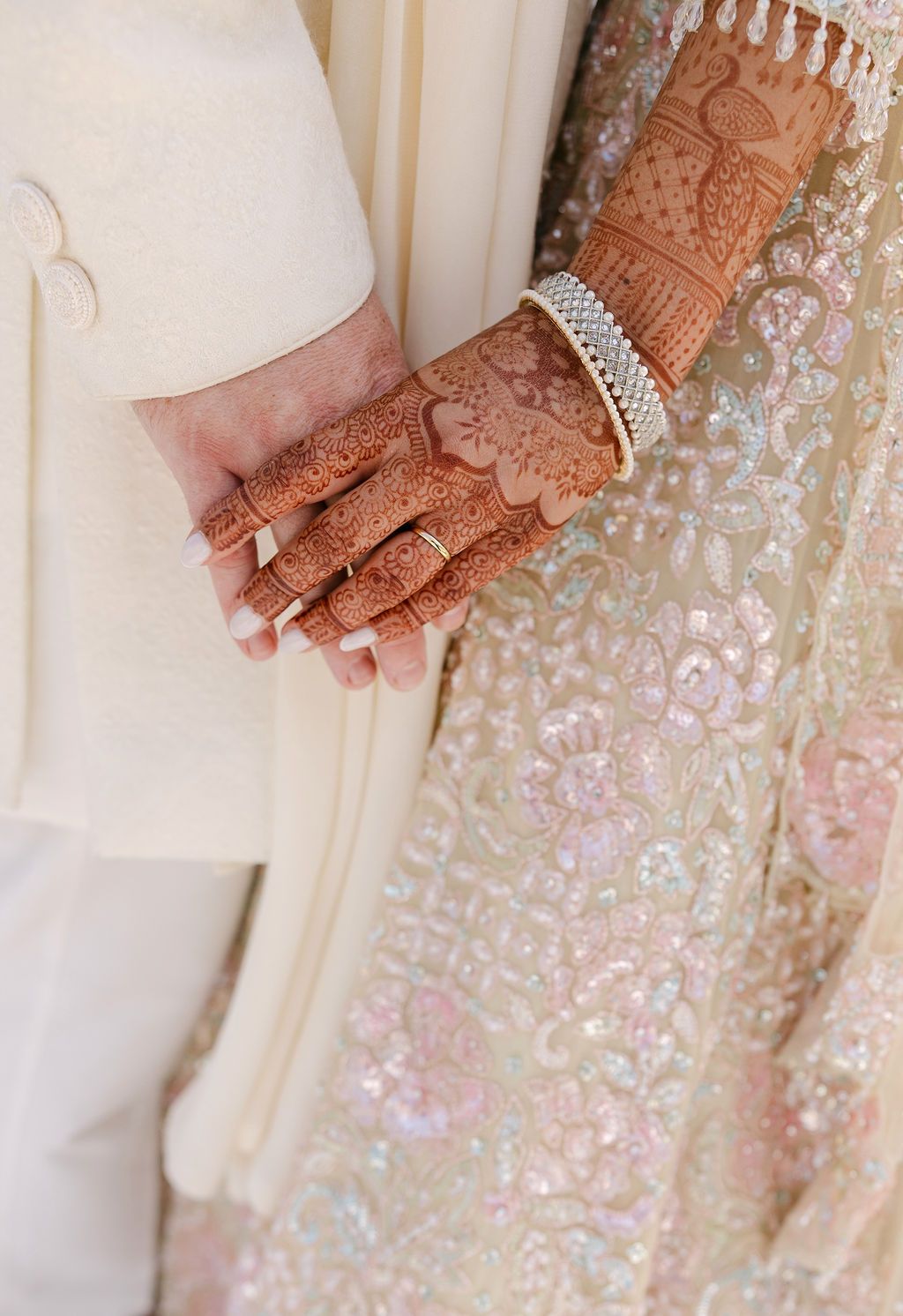 Detailed shot of intricate henna design on hand with diamond bracelet against embroidered fabric.