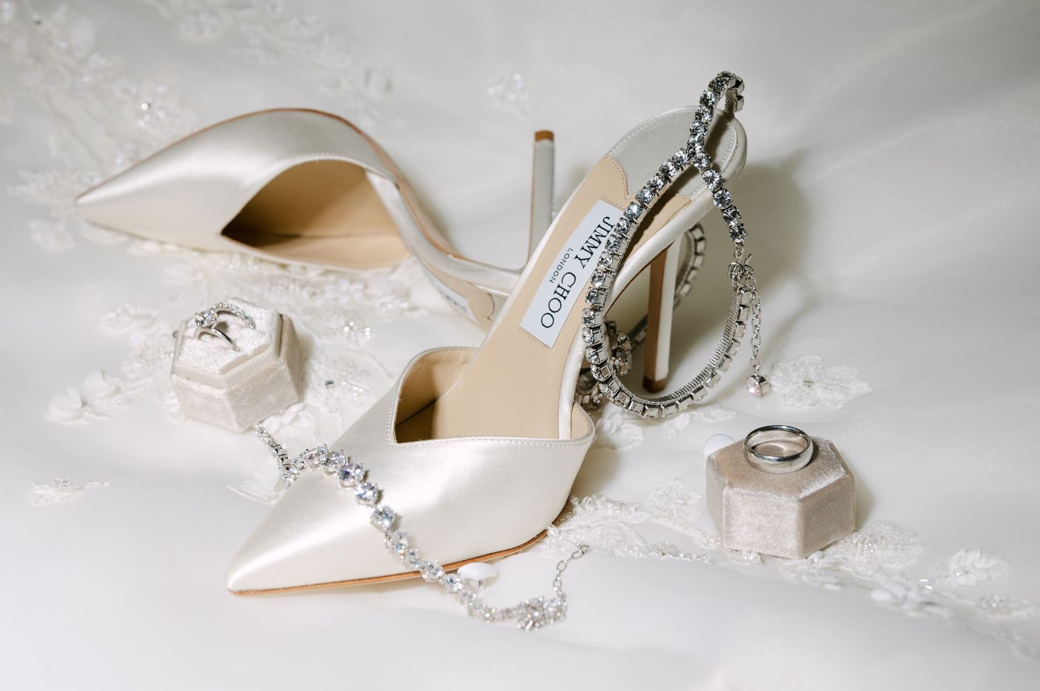Elegant white bridal shoes with crystal details and jewelry on lace background.