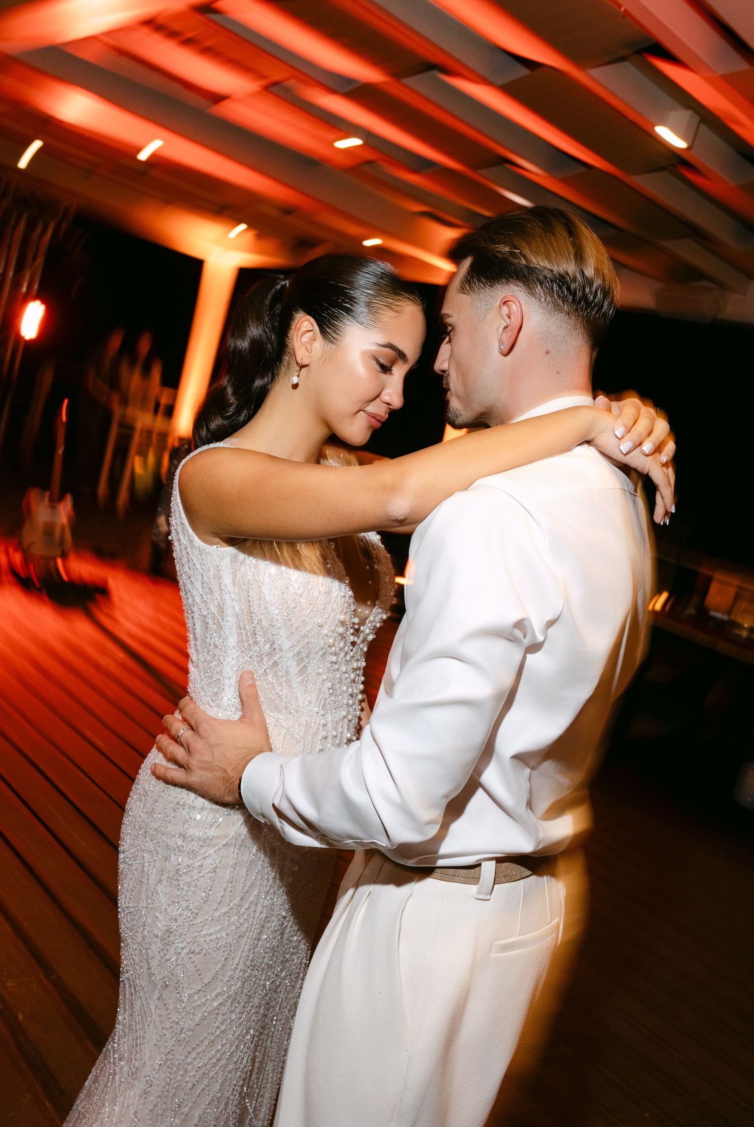 Couple sharing romantic dance under warm red lighting at wedding reception.