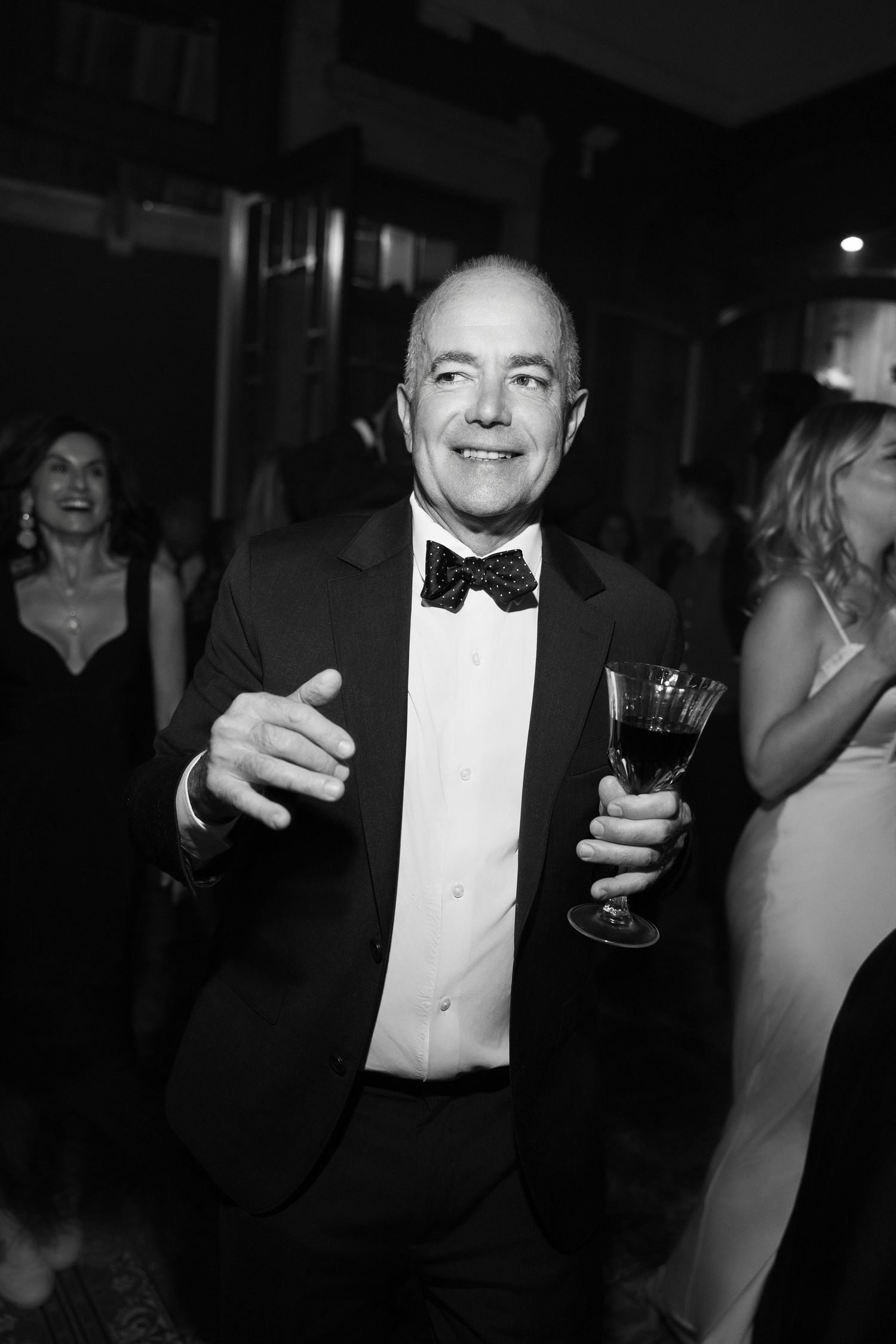 Formal event guests in black tie attire enjoying drinks at evening celebration.