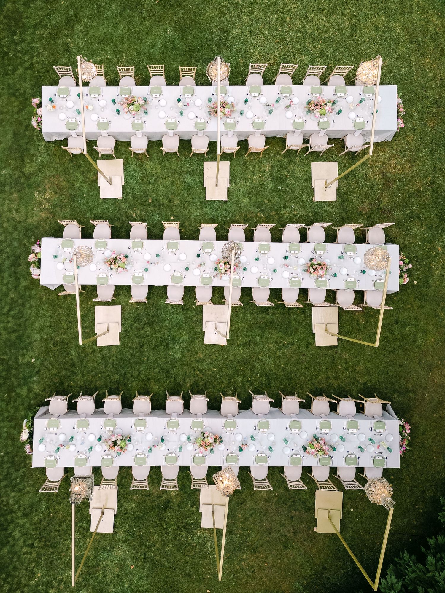 Aerial view of elegant white wedding reception tables arranged on a green lawn.
