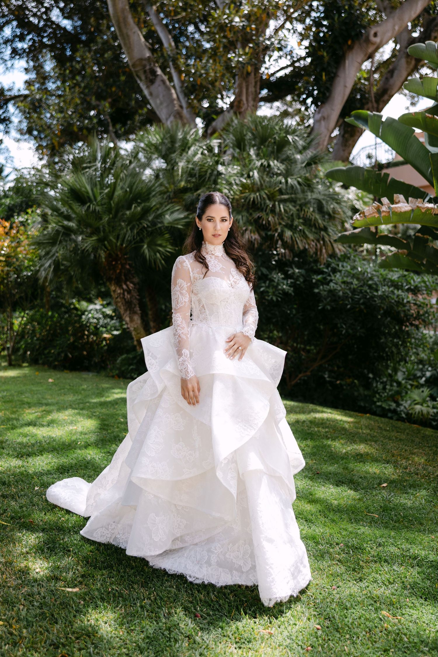 Bride in lace gown twirls gracefully in garden setting with natural lighting.