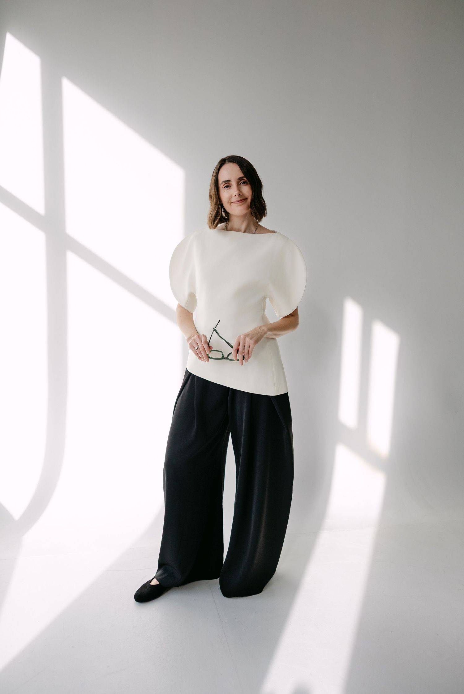 Fashion series capturing movement and style with white top and black pants in bright studio space.